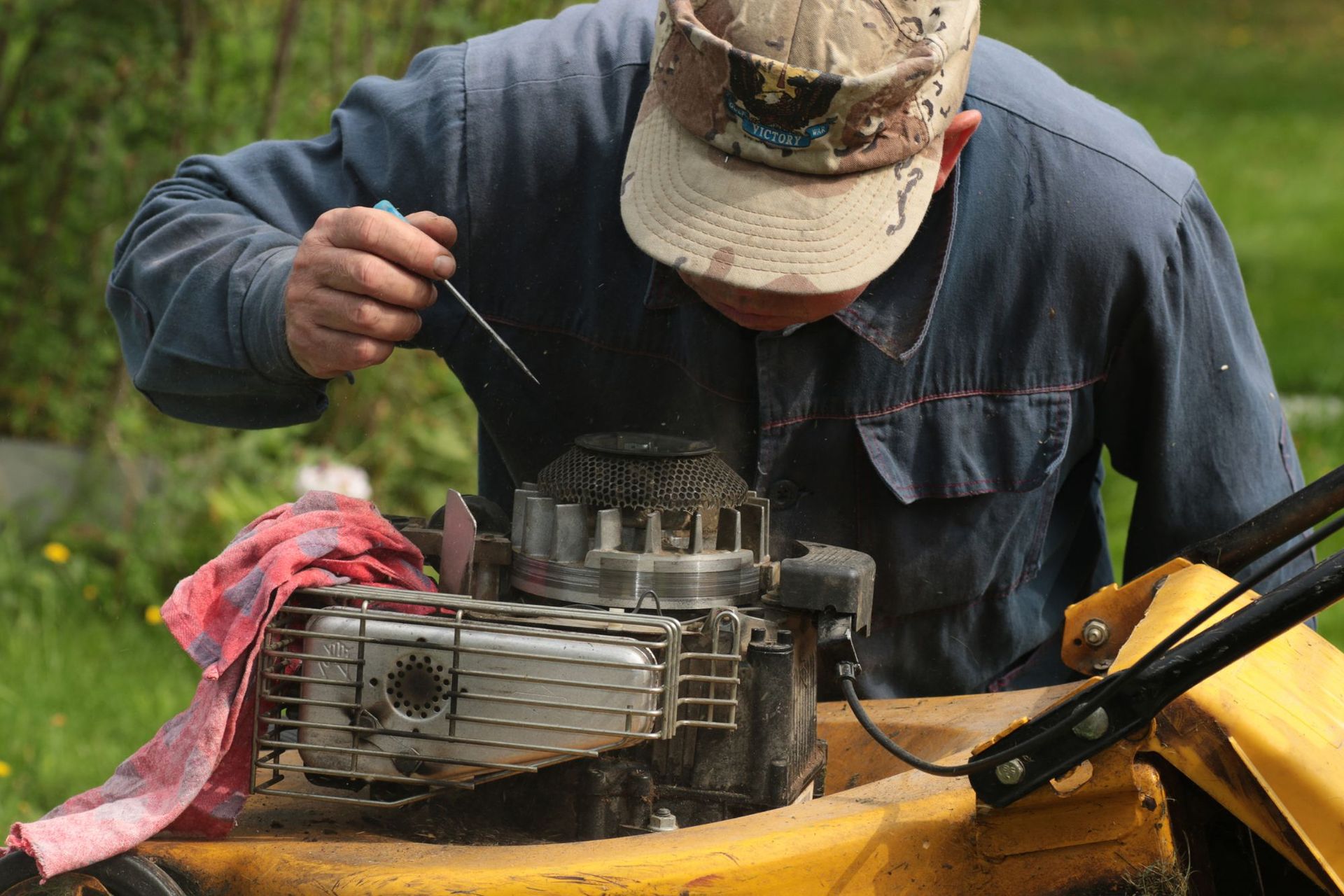 A man is working on a lawn mower with a screwdriver.
