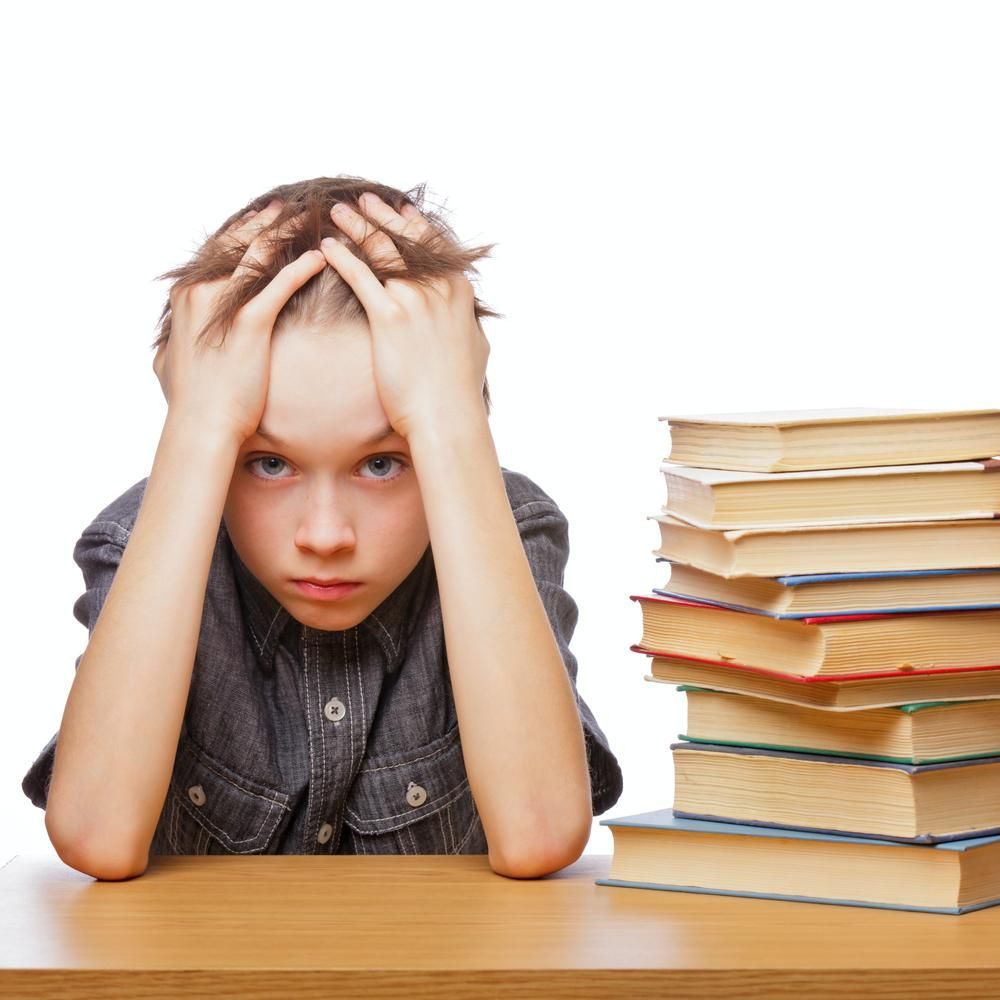 A Young Boy Sits at A Desk with His Hands on His Head in Front of A Stack of Books — Al Roberts Education Centre in Wynnum West, QLD