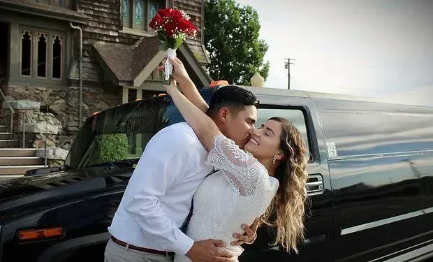A bride and groom are kissing in front of a truck.