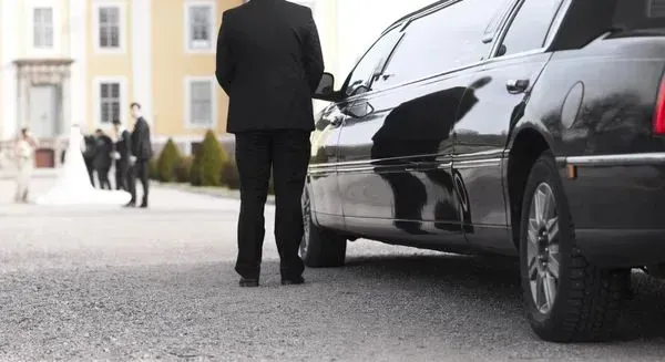 A man in a suit is standing next to a black limousine.