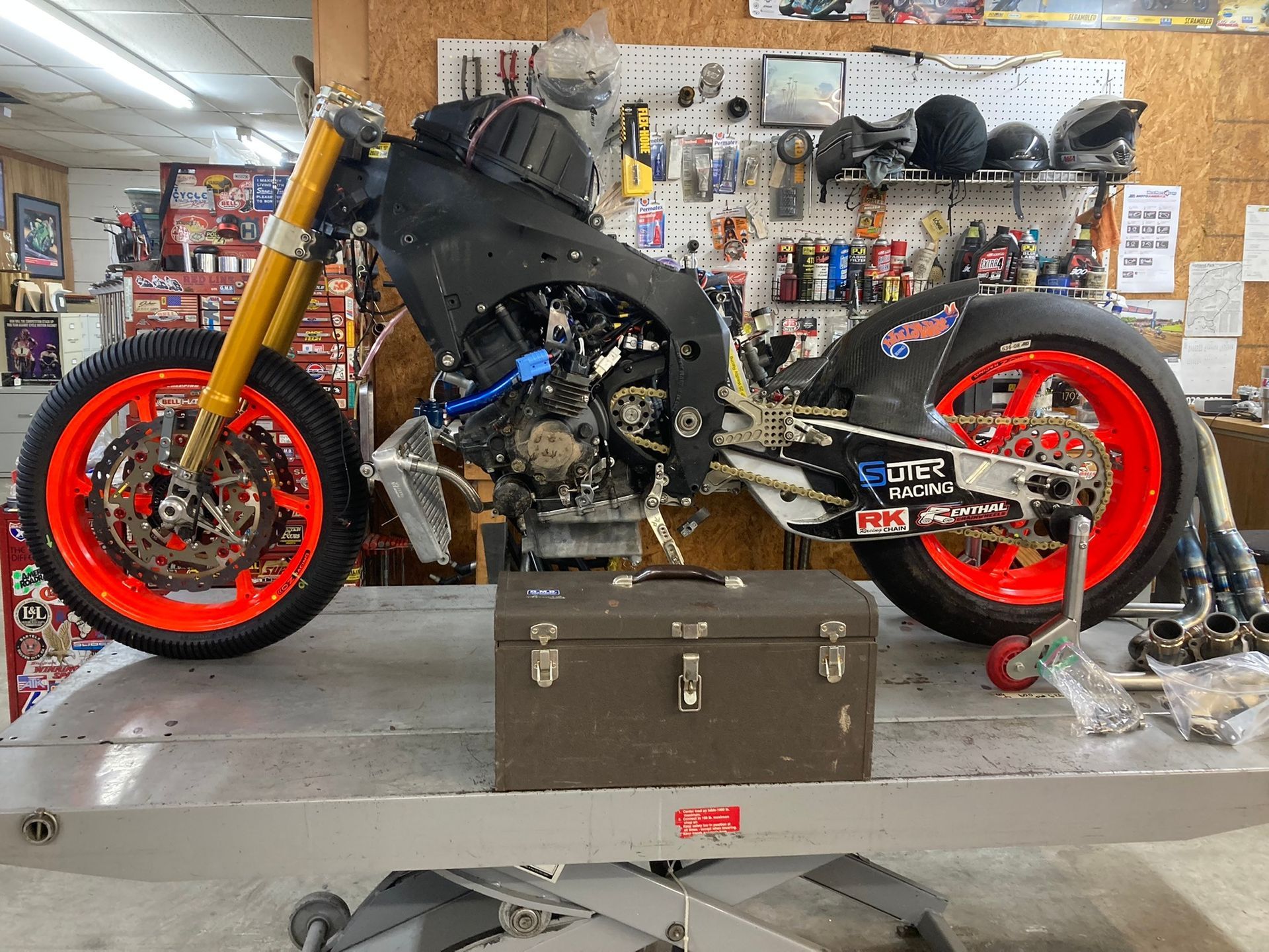A motorcycle with red wheels is sitting on a lift in a garage