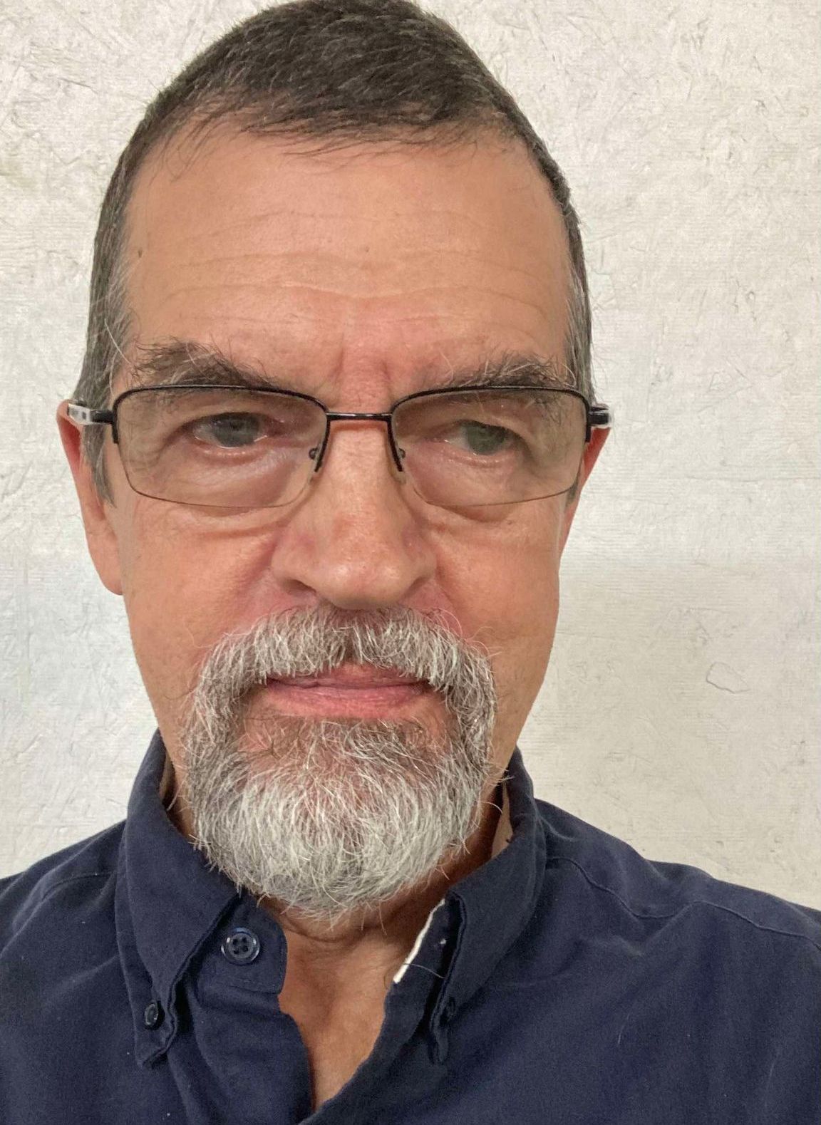 A man with glasses and a beard is wearing a blue shirt.