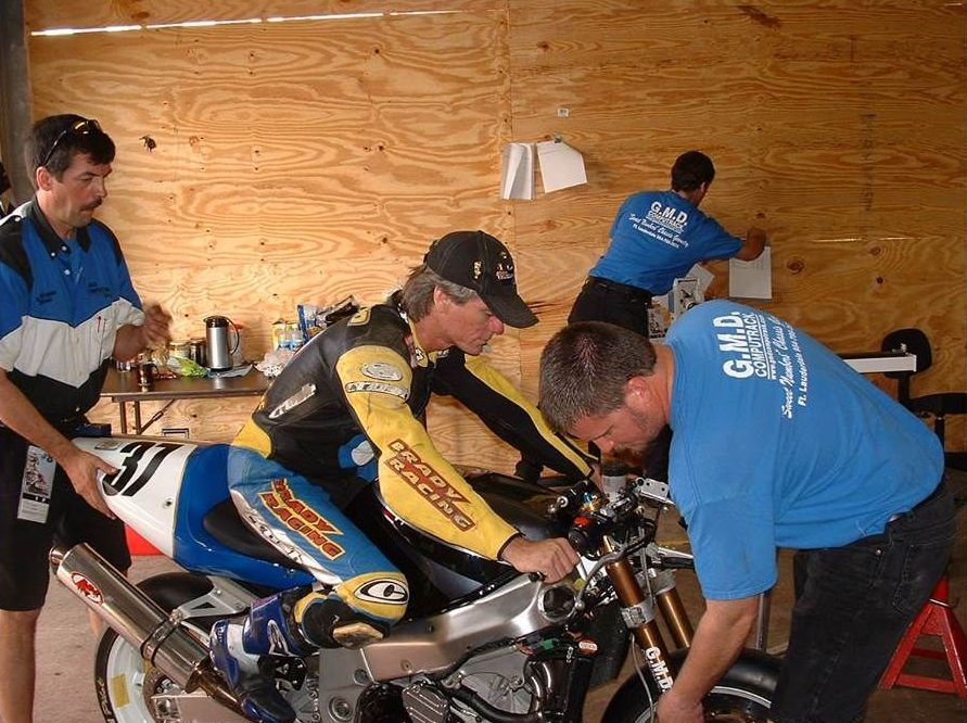 A man wearing a blue shirt that says gulf coast is working on a motorcycle