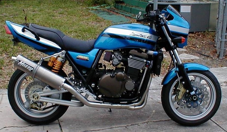 A blue and white kawasaki motorcycle is parked on the sidewalk