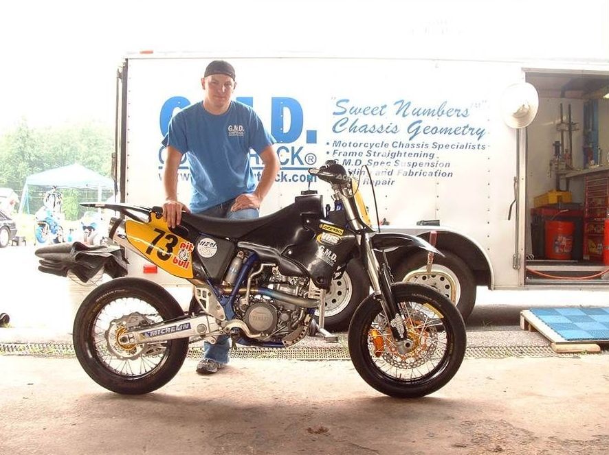 A man stands next to a dirt bike with the number 73 on it