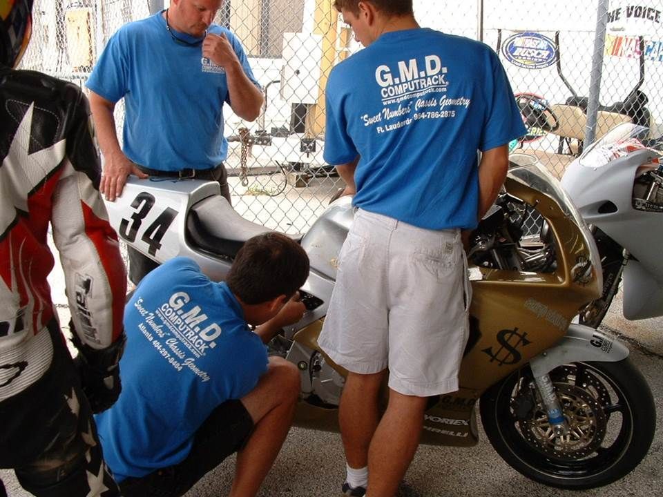 A man wearing a blue shirt that says g.m.d. is working on a motorcycle
