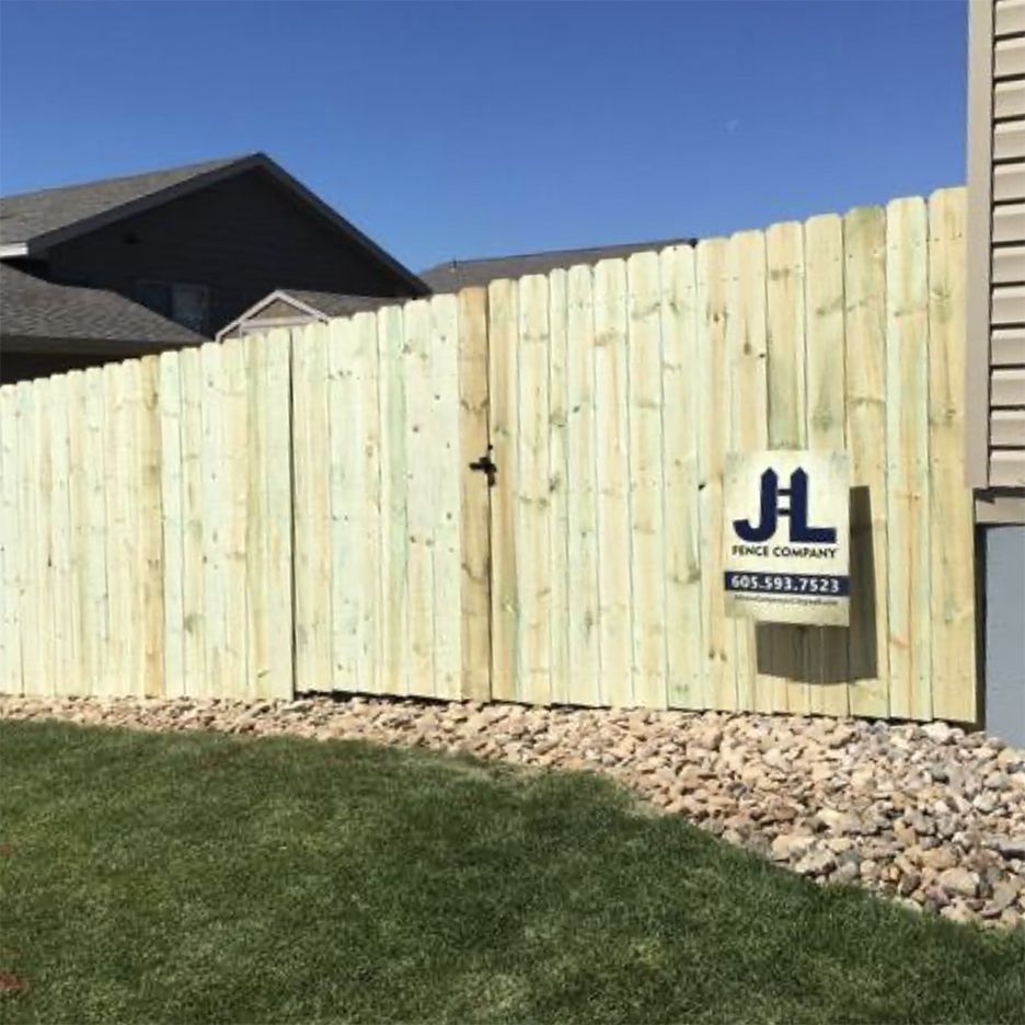 Wooden fence with a gate, green grass, and a sign. Blue sky in the background.