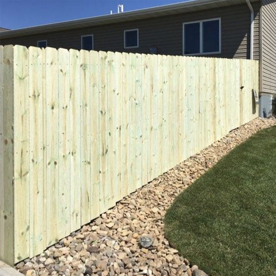 Wooden privacy fence alongside a house with gravel and grass.
