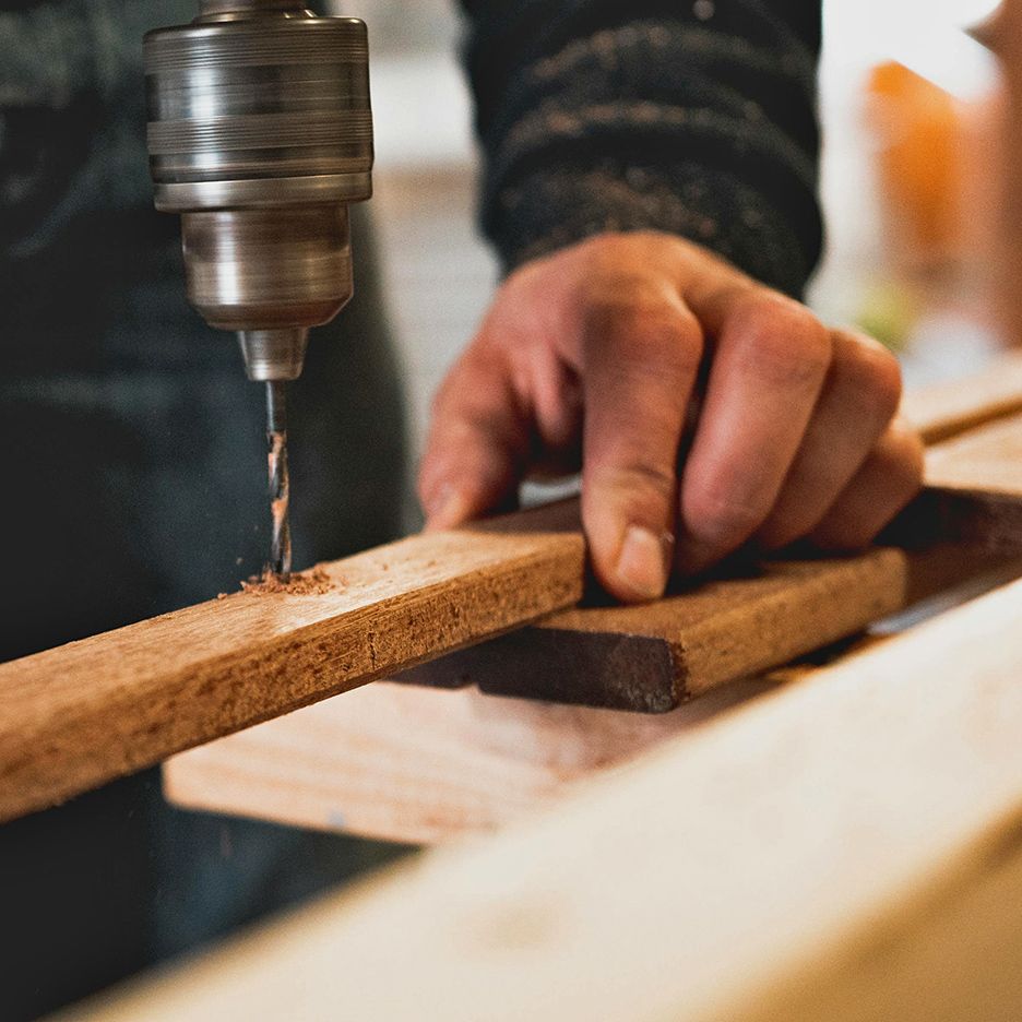 A person drilling a hole into a piece of wood with a power drill.