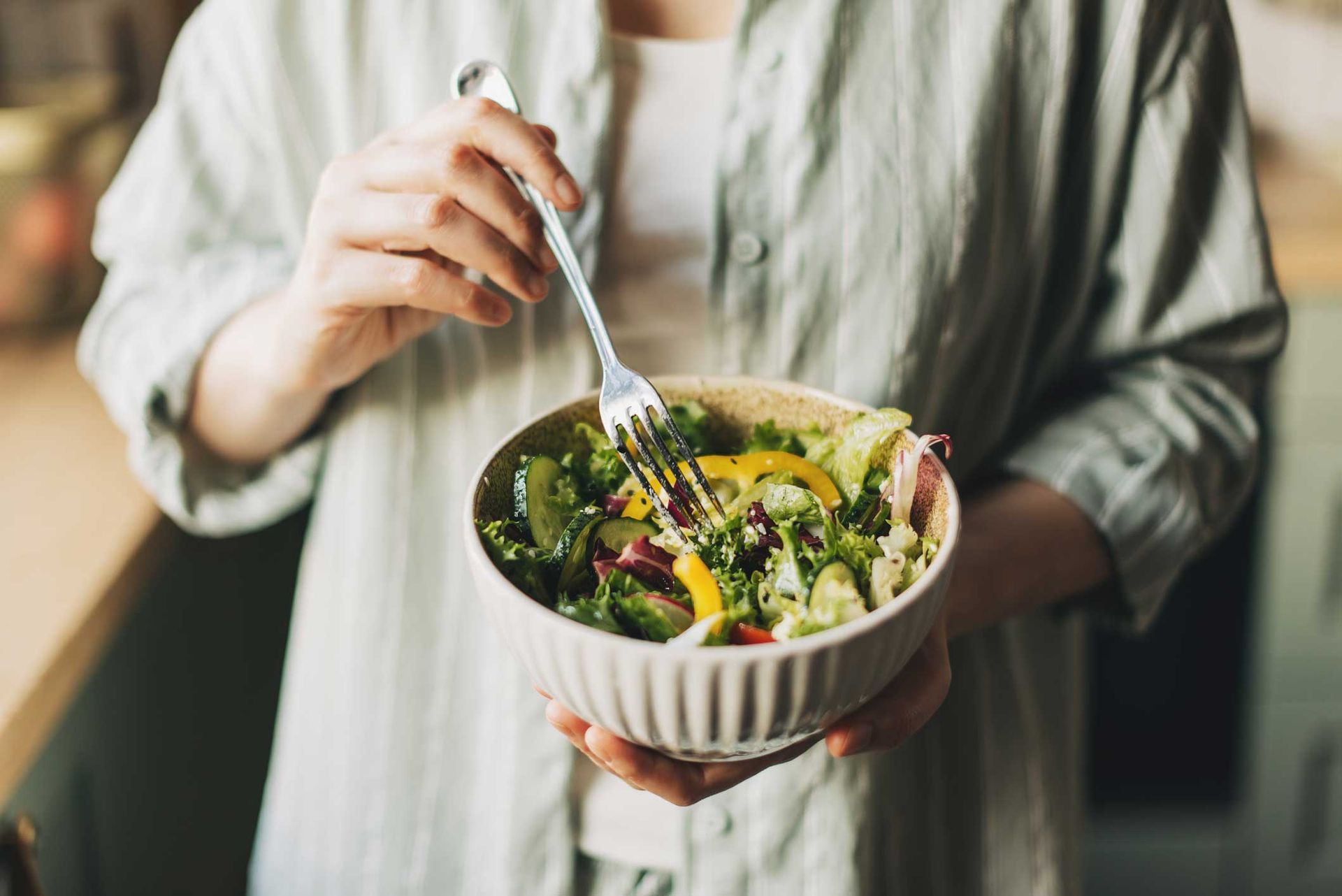 Person holding a bowl of salad, preparing to eat; green shirt, kitchen setting.