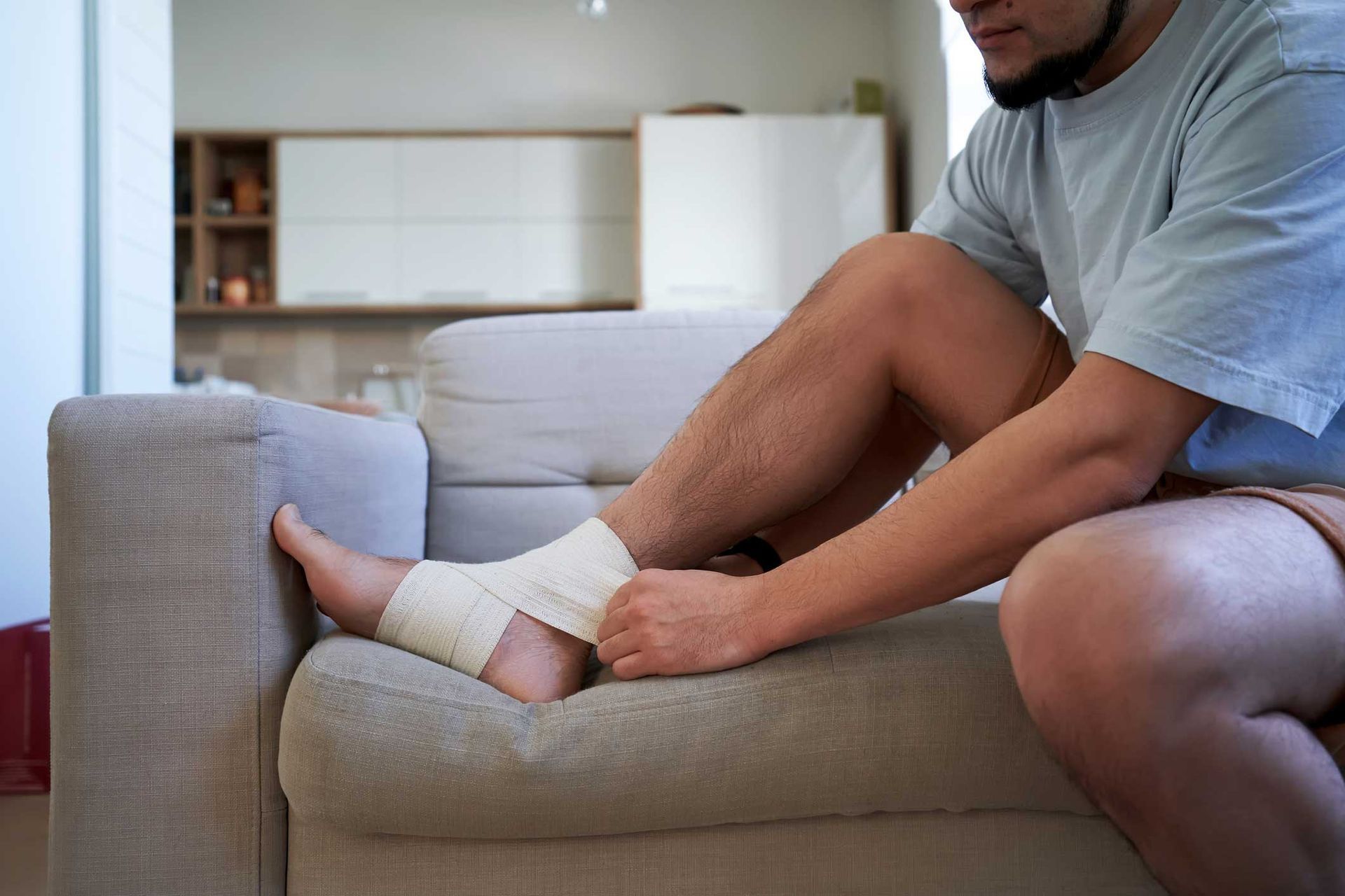 Man wrapping ankle with bandage on a couch.