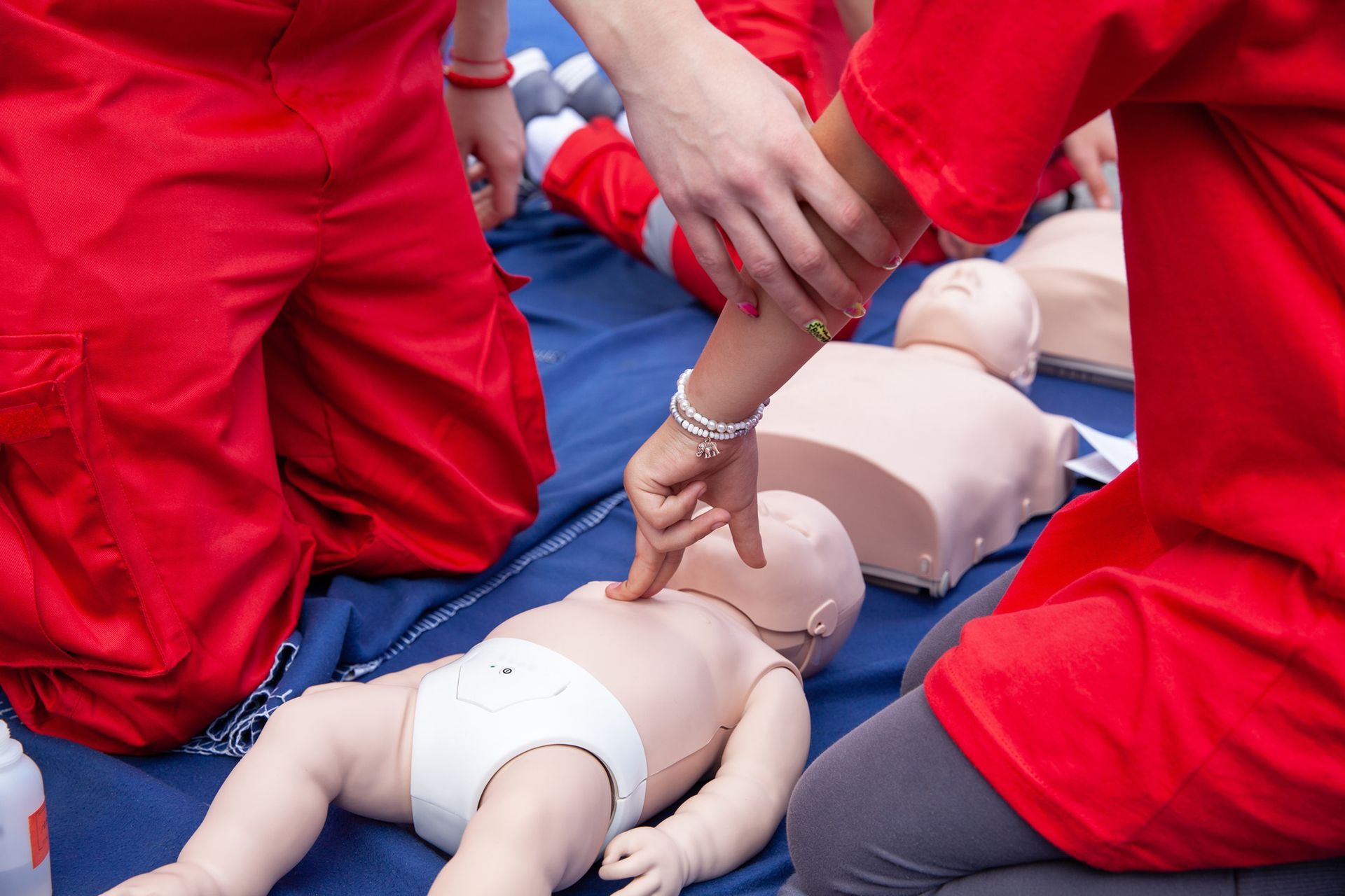CPR instructor demonstrating on a dummy, surrounded by seated students in a classroom.