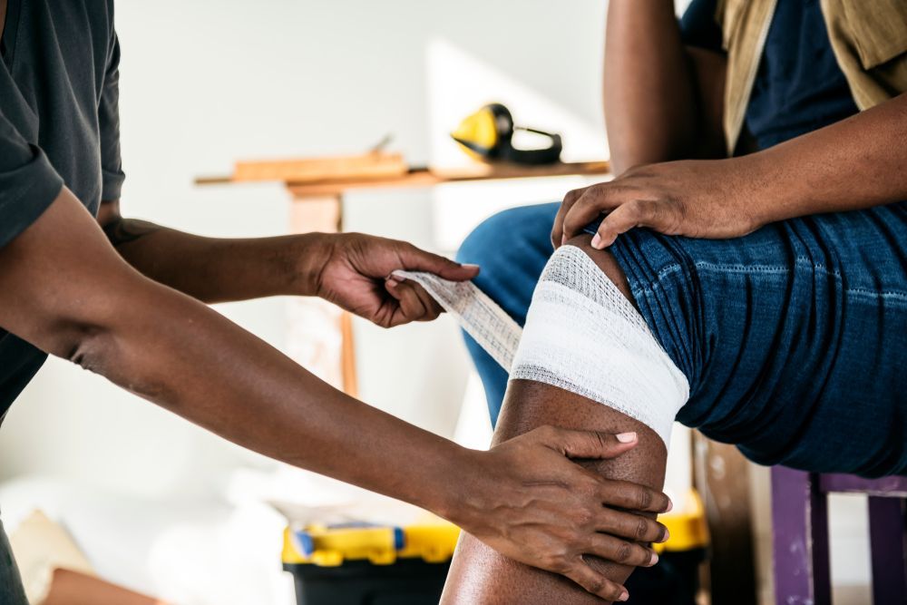 Person wrapping a bandage on a knee wound. A construction setting.