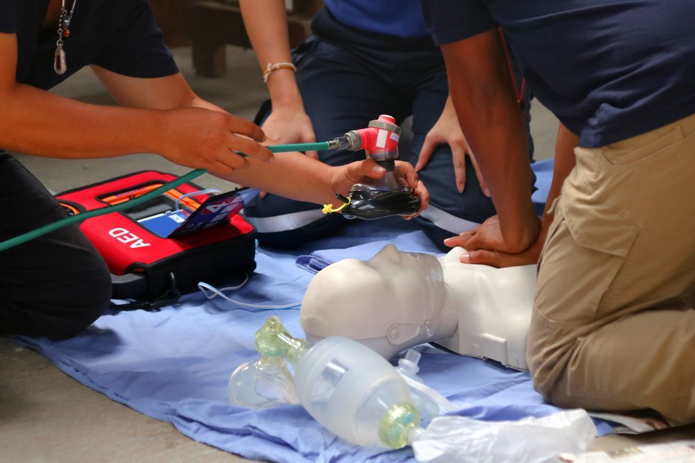 People practicing CPR on a mannequin, with an AED and medical equipment nearby.