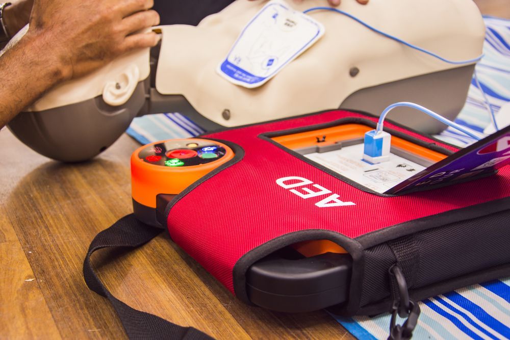 AED training demonstration: Hands on chest of mannequin, red AED bag in foreground.