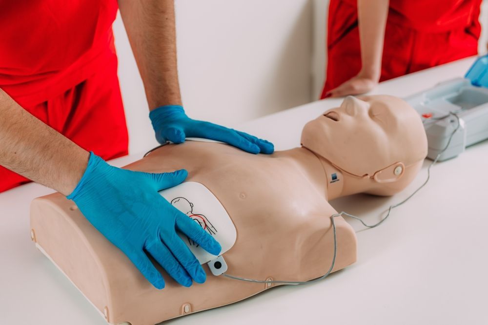 CPR training dummy with person practicing chest compressions and AED pads attached.