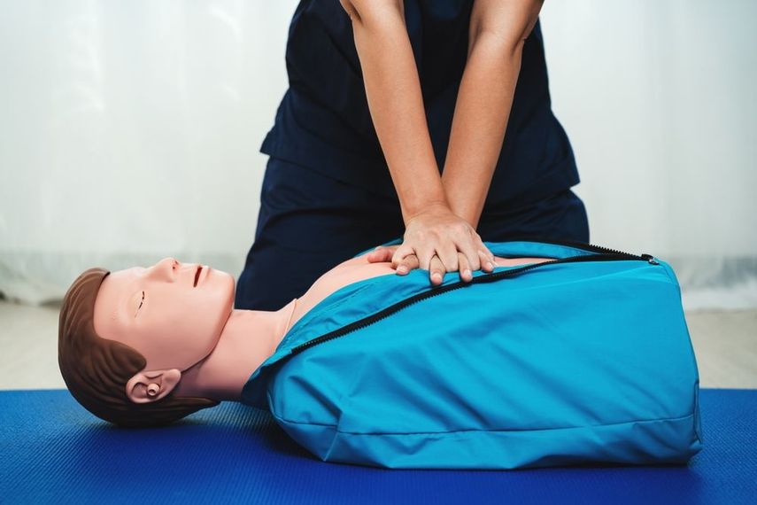 Person performing CPR on a mannequin, indoors. Hands clasped, chest compressions.