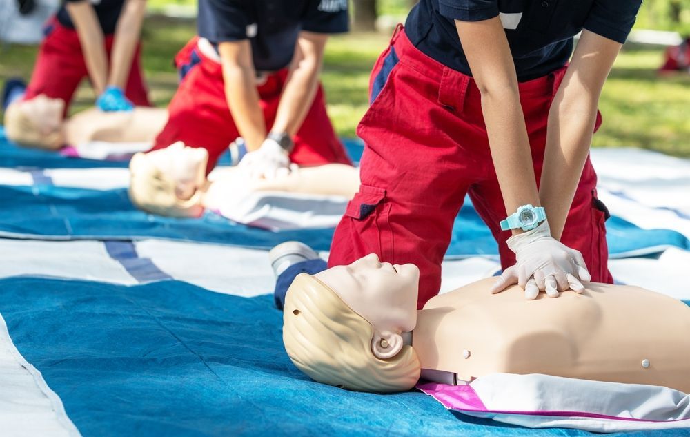 People in red pants and blue shirts practicing CPR on mannequins outdoors.