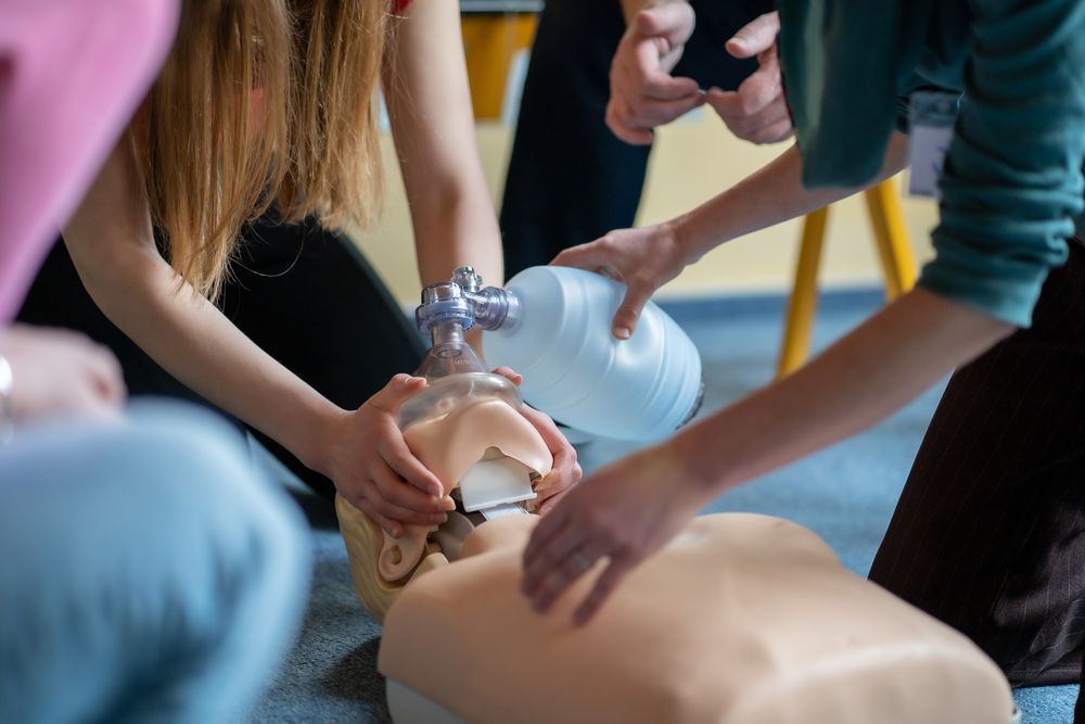 CPR training session; hands using a bag valve mask on a mannequin.