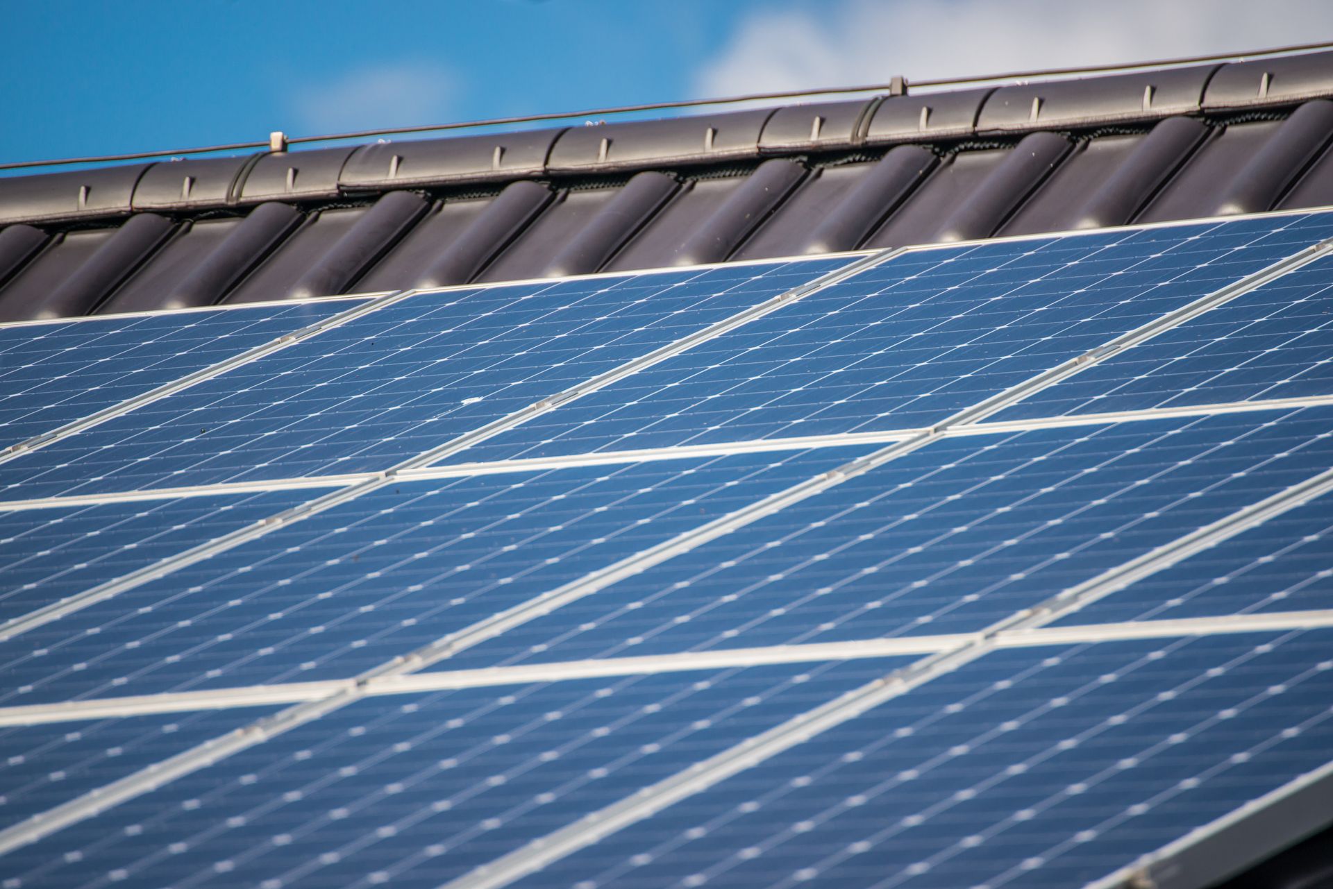 Blaue Solarpaneele, die auf einem Wohnhausdach vor einem sonnigen, blauen Himmel installiert sind.