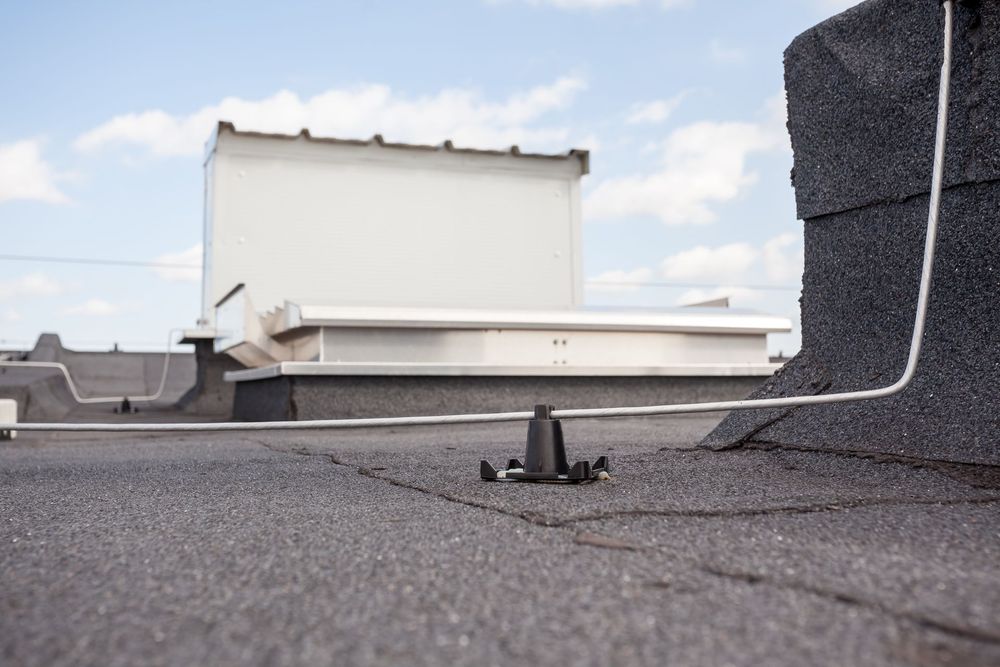 Ein Metalldraht verläuft entlang eines flachen, dunklen Daches und wird von einem schwarzen Kunststoffständer gehalten