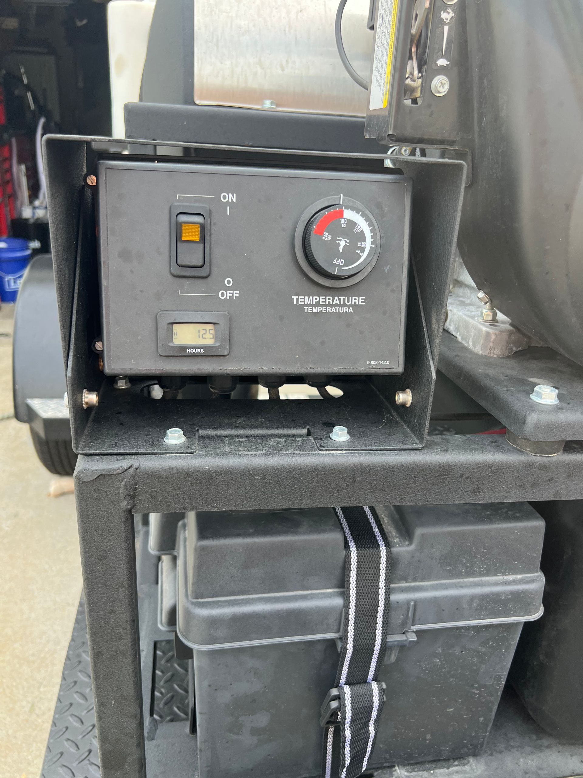 A black control panel with an on/off switch, a temperature dial, and a digital display is mounted above a battery box secured by a strap.