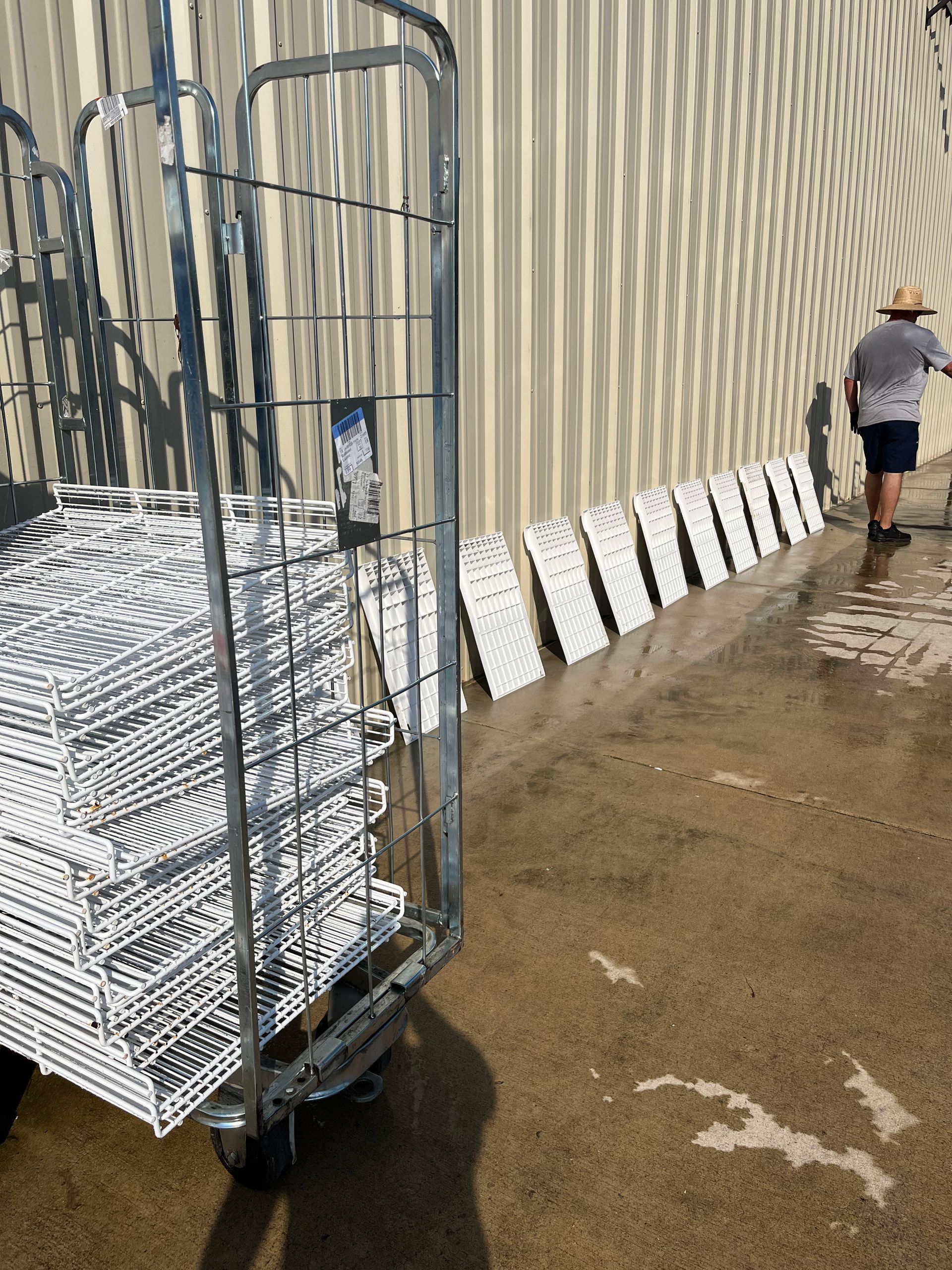 A metal cart loaded with stacked white wire baskets stands near a wall with a row of matching baskets. A person is visible in the background.