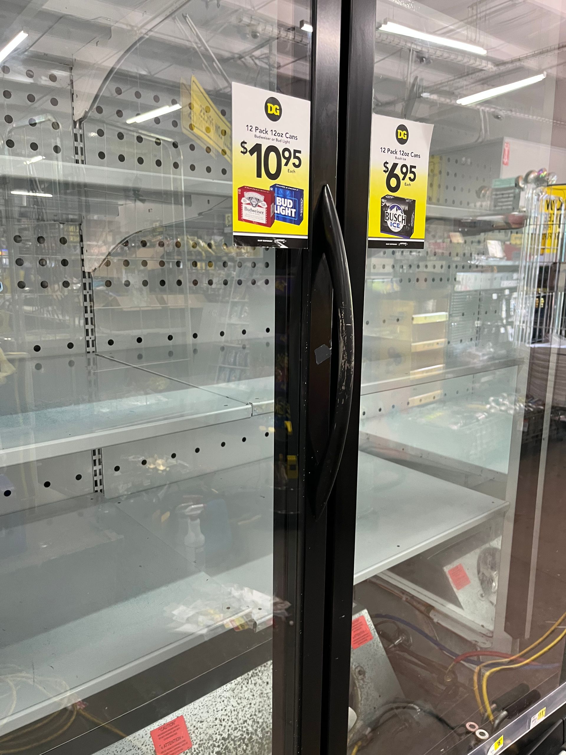 Empty refrigerated shelves in a grocery store. Two price tags hang on the glass door.