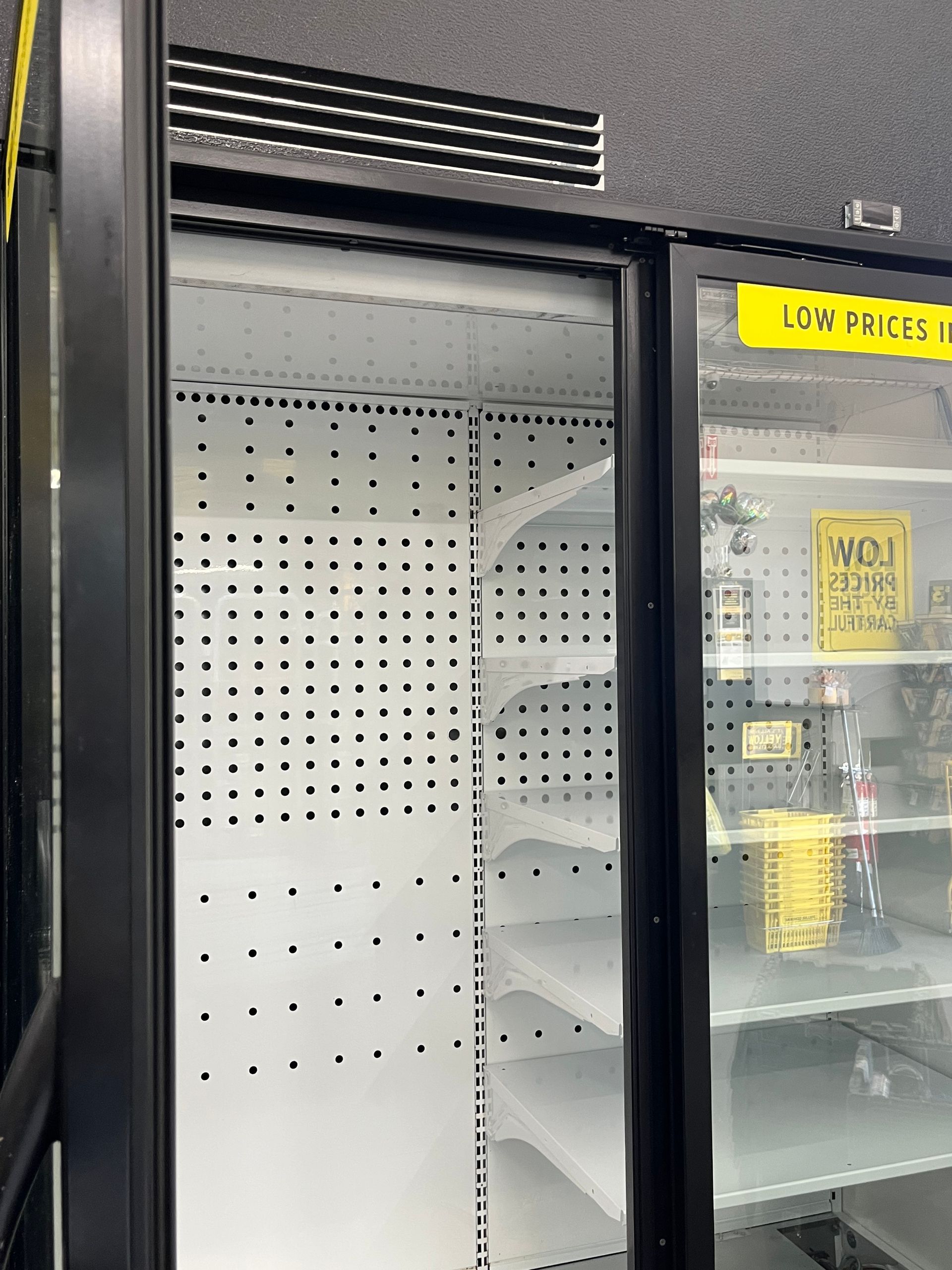 Empty white refrigerator with black trim, ajar. A partially visible refrigerator with items inside is to the right.