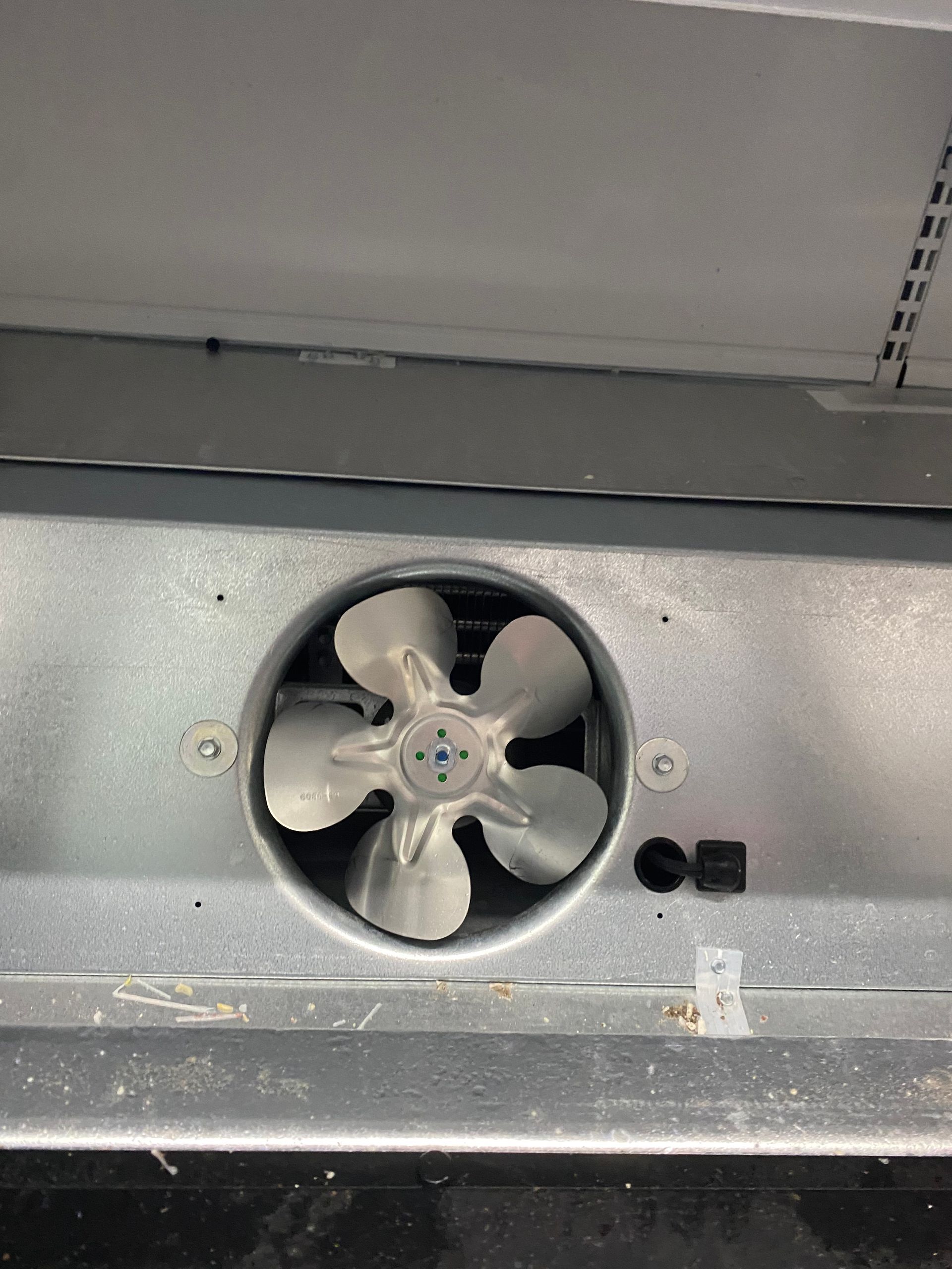 A close-up view of a fan within a metal housing. The fan has five blades and appears to be inside an appliance.