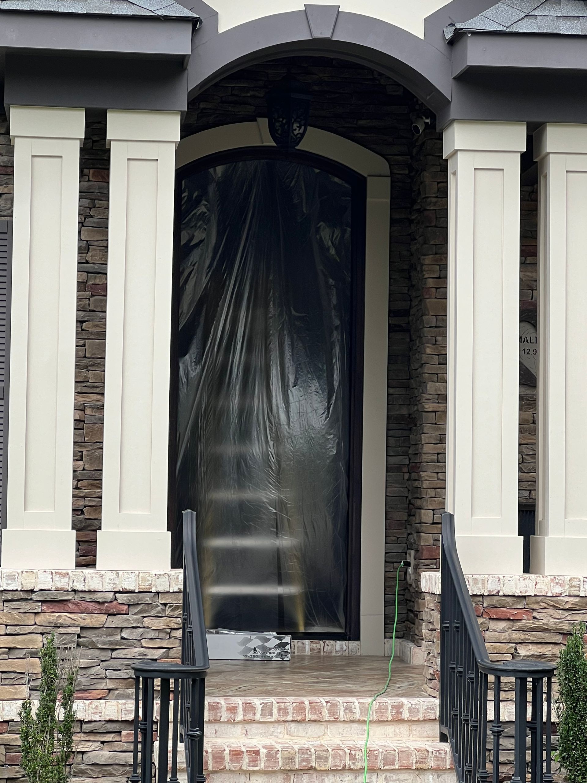 A covered doorway on a home with stone and white columns. The door is covered in black plastic.