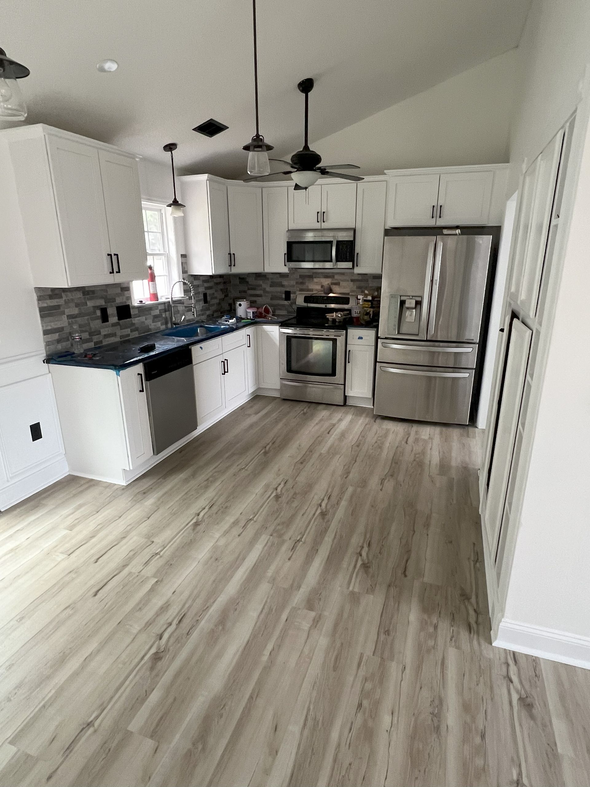 Modern kitchen with white cabinets, stainless steel appliances, and light wood-look flooring. Blue countertops and a gray backsplash complete the space.