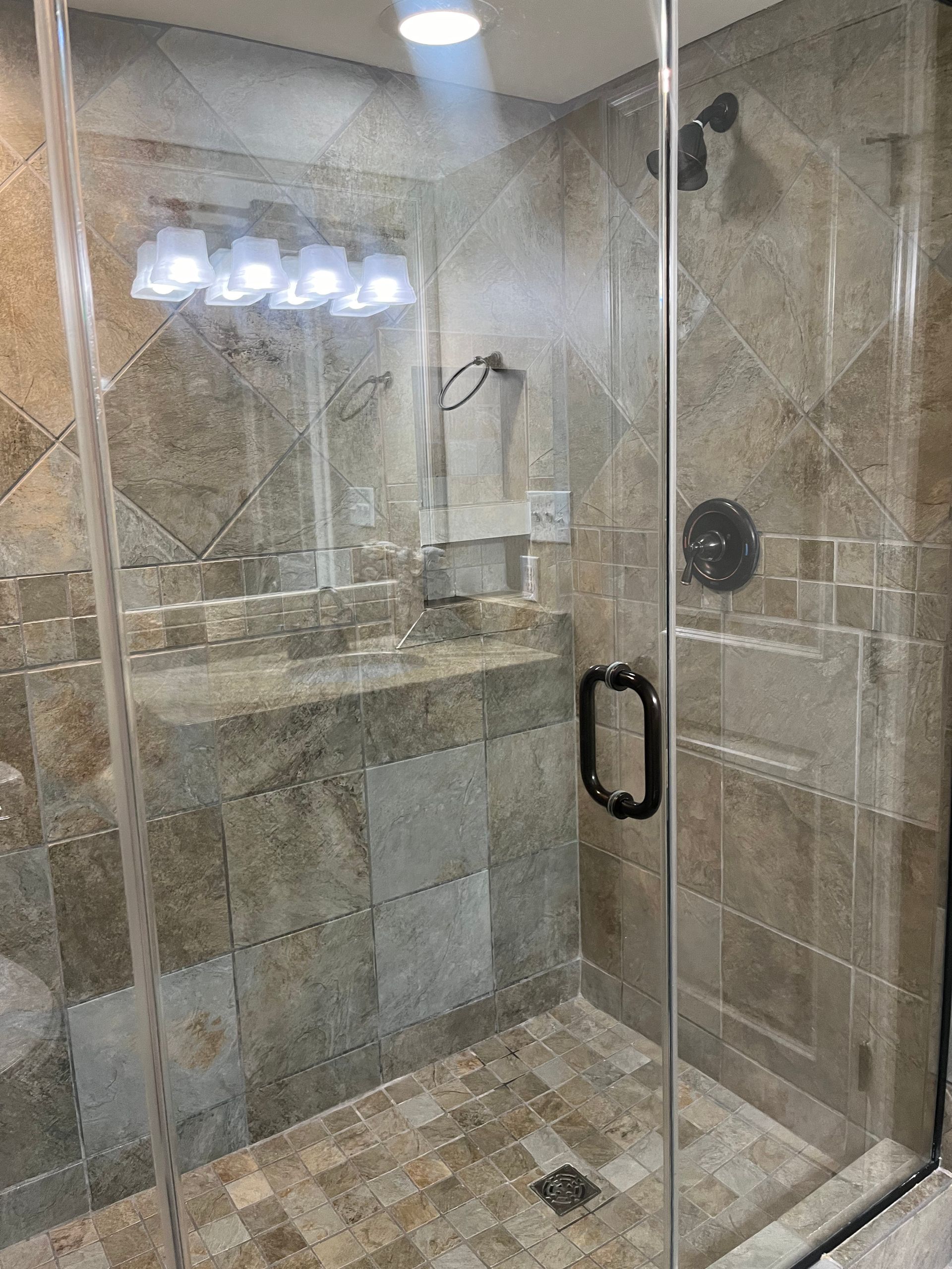 A bathroom with a glass shower, tan tile walls, a sink, and a mirror. The setting is well-lit with a modern design.