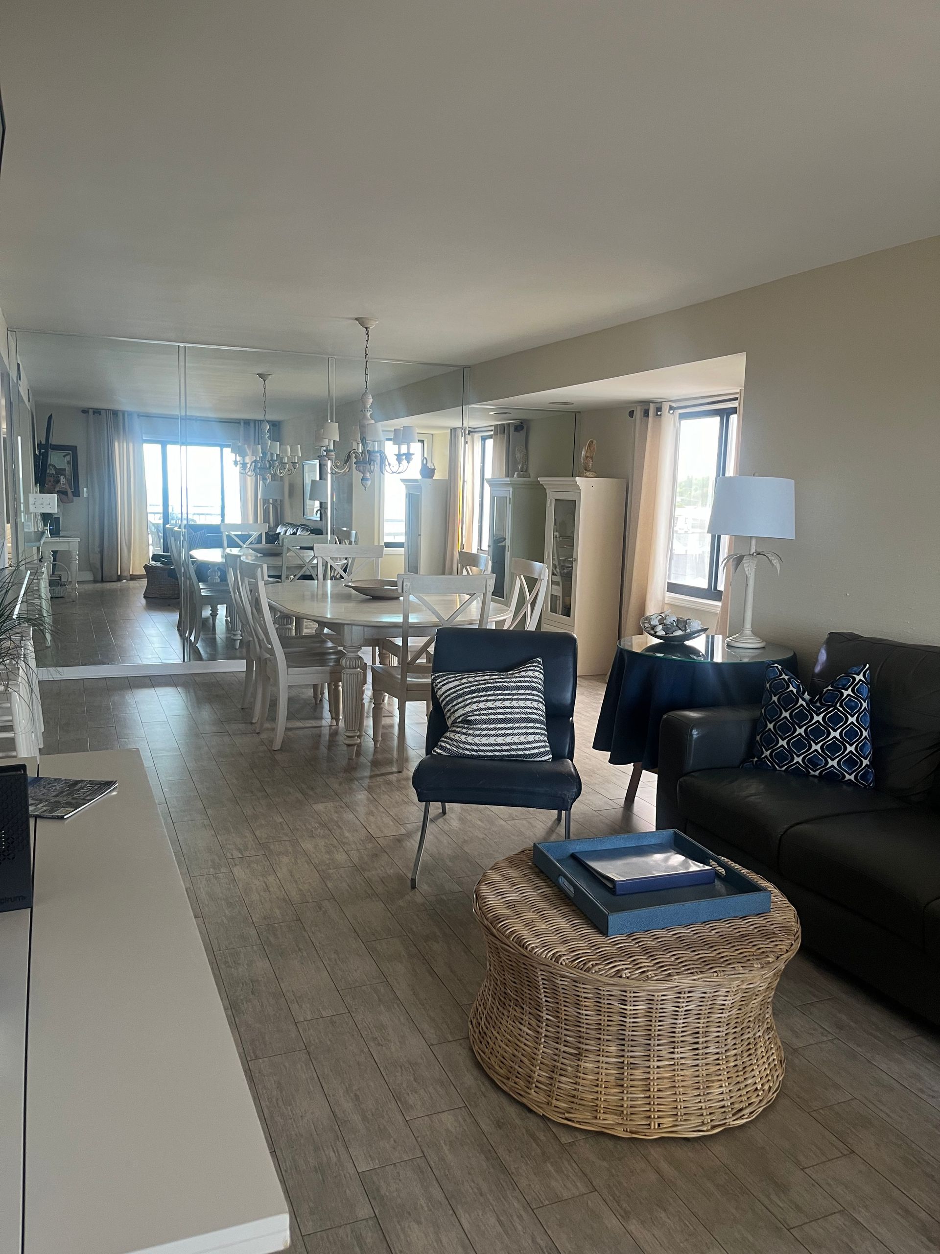 Living room with light wood floors, white walls, and a large dining table near a window with a view. A dark sofa and blue accent chair sit nearby.