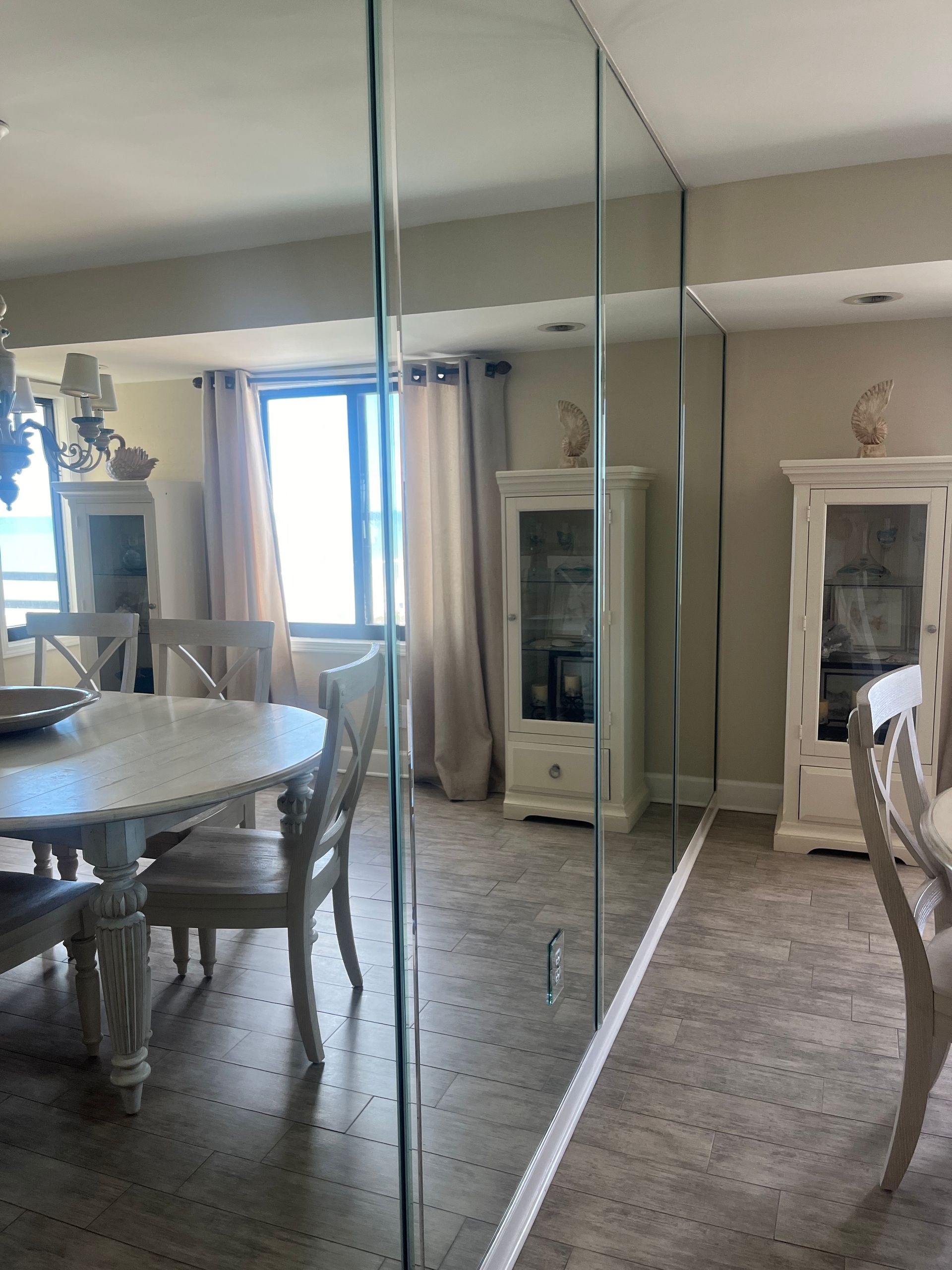Dining room with a large mirrored wall, a round white table, and white chairs. Two white display cabinets are visible.