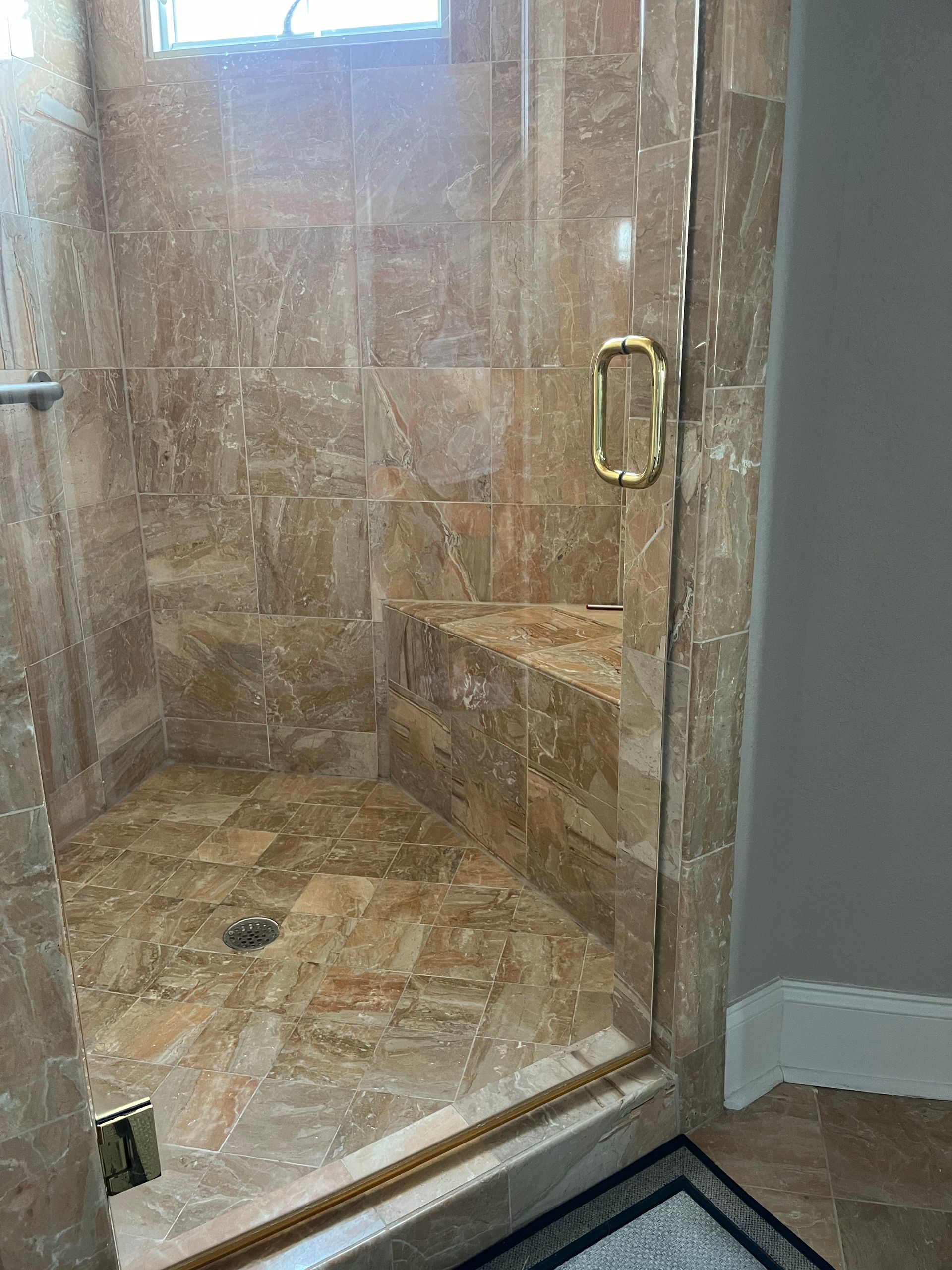Tile-walled shower with glass door, gold-toned fixtures, and built-in seat. The tile is a warm brown color.