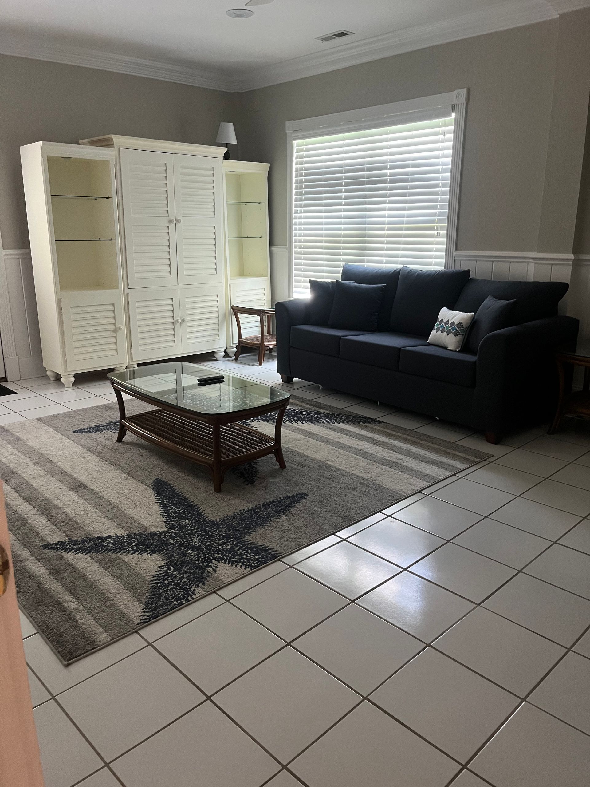 Living room with white tile floor, gray sofa, a rug with a starfish design, and white cabinets.