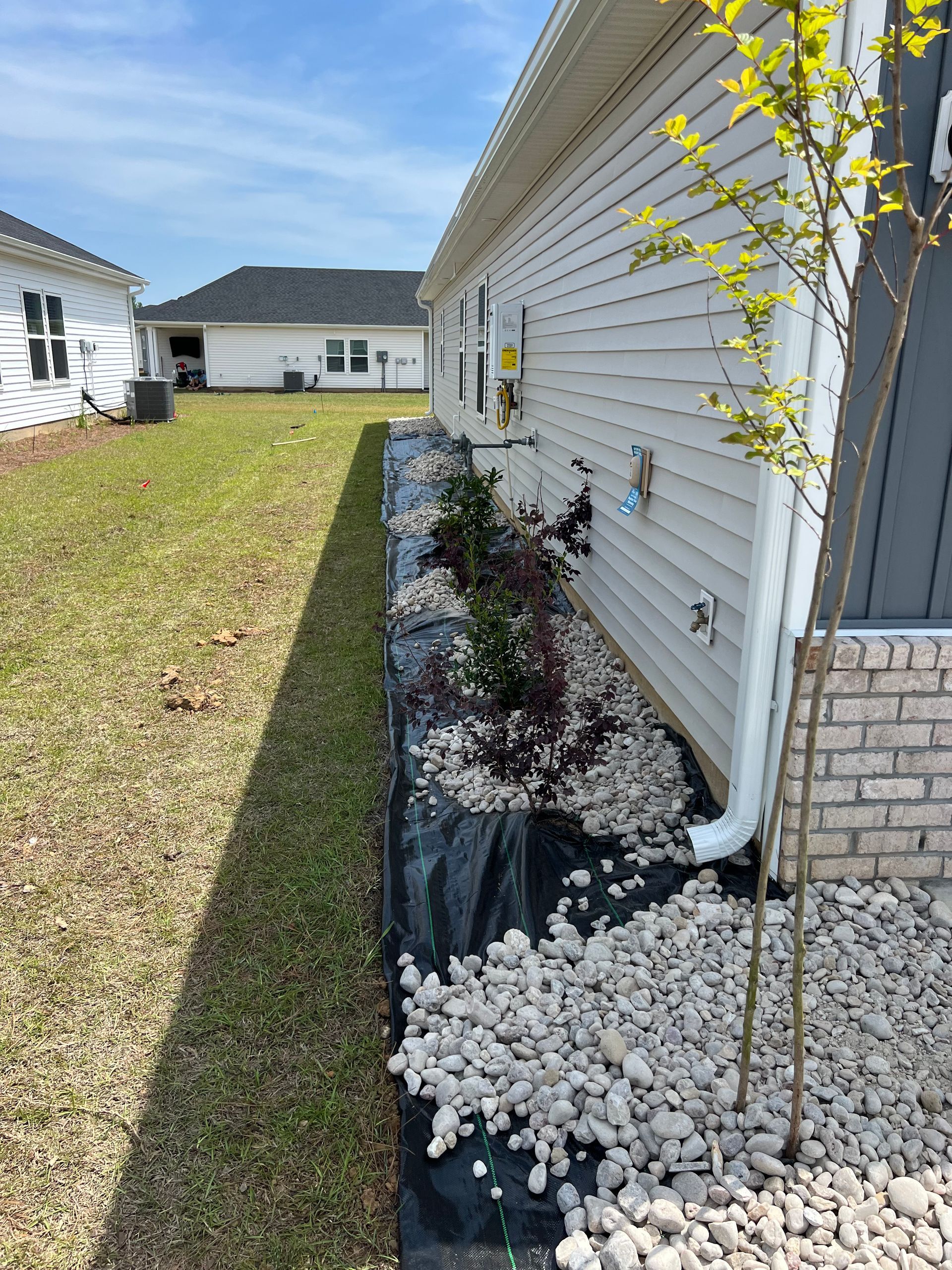 A house exterior with a planted bed of shrubs and a rocky border next to a grassy area.