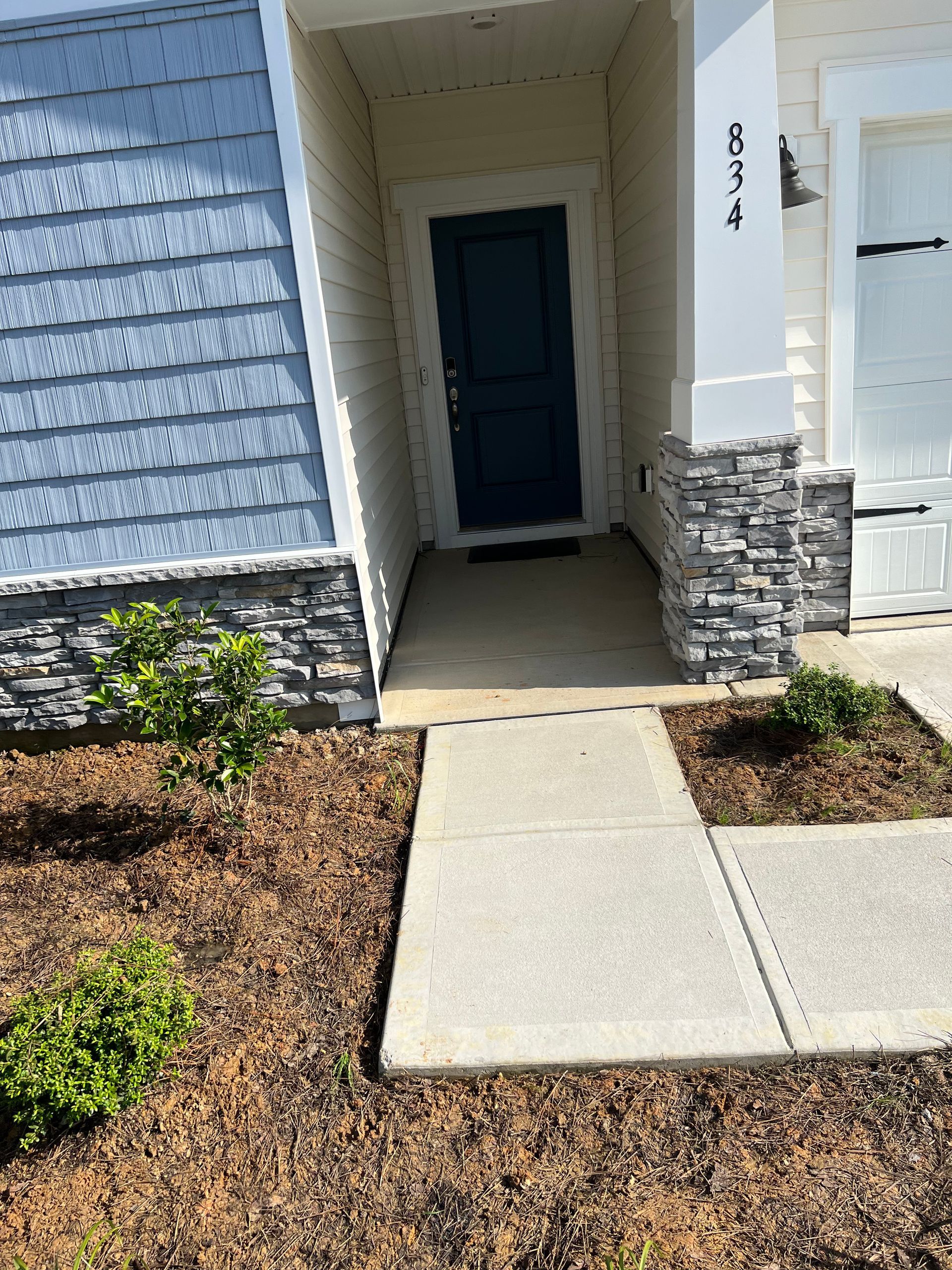 Front entrance of a house with blue siding and a dark blue door. A concrete walkway leads to the entrance.
