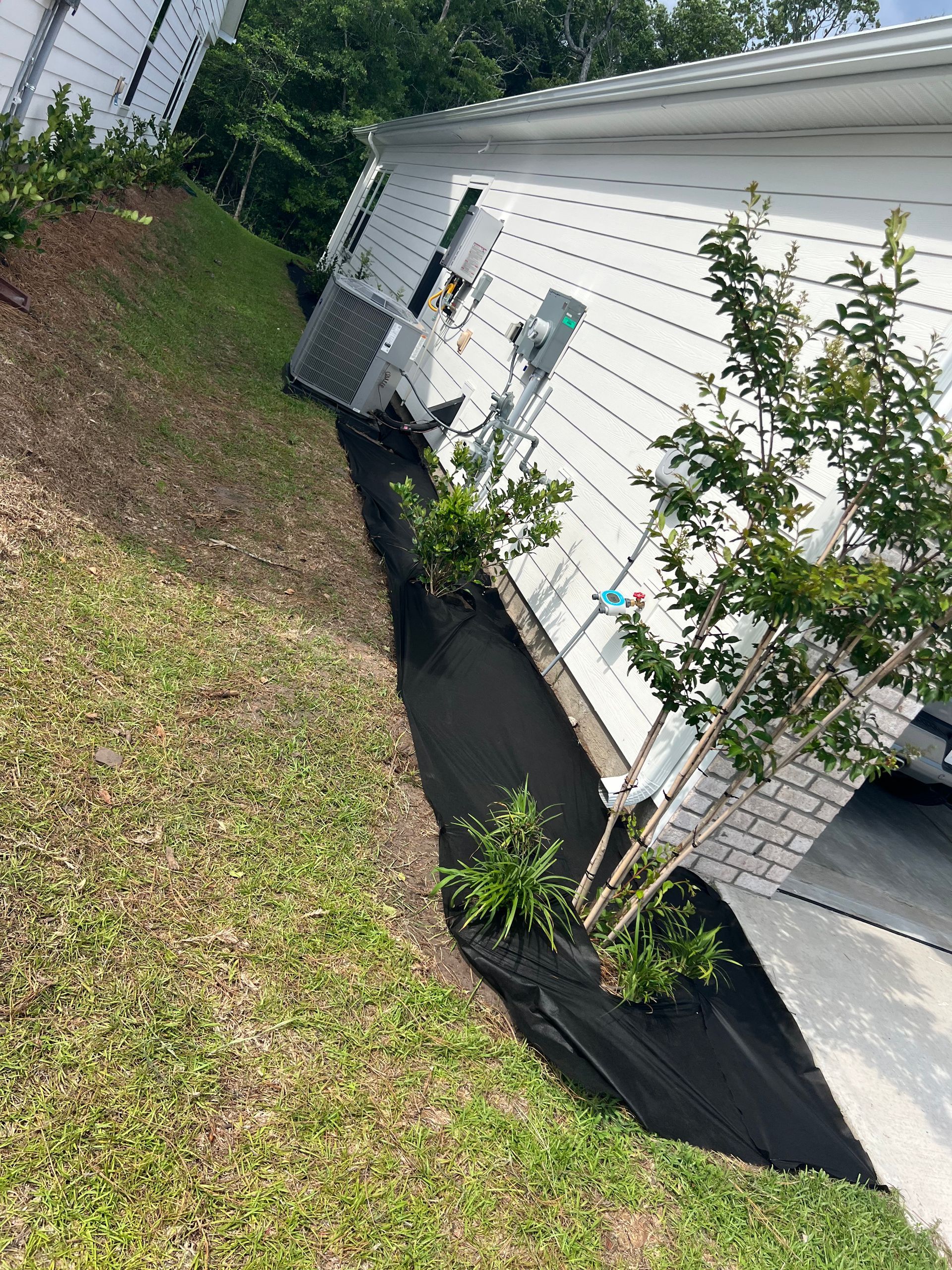 A white building with a black strip of landscaping, small green plants, and an air conditioning unit along the side.