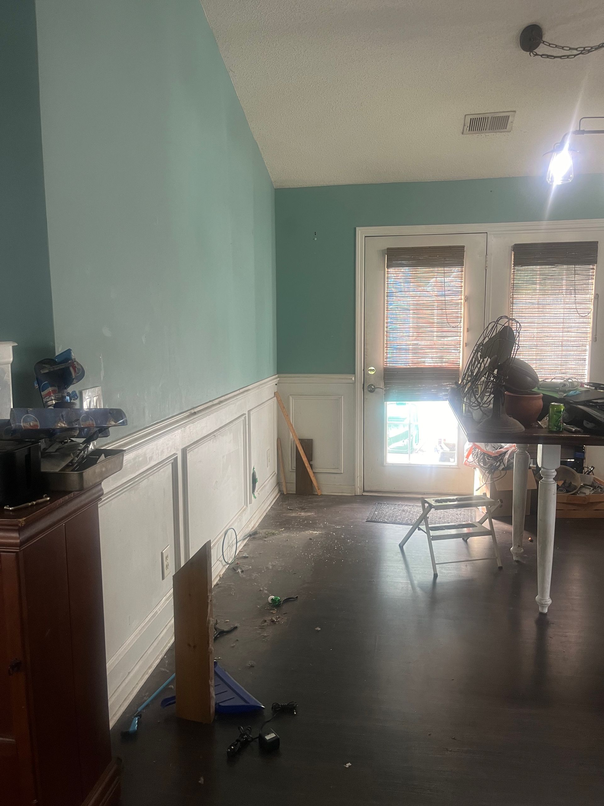 A room with teal walls, white wainscoting, and dark wood floors. A door leads outside, and furniture is present.