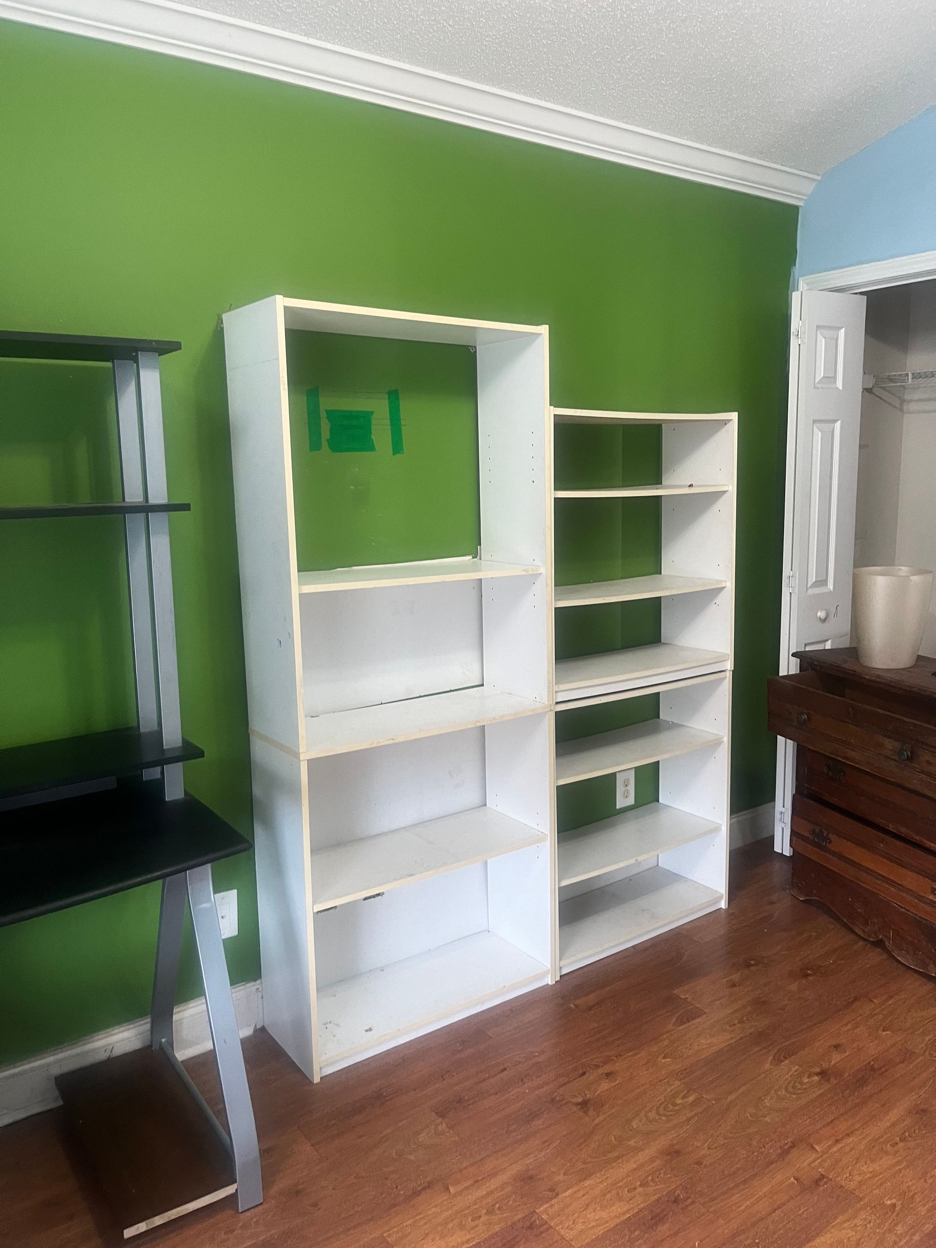 White bookshelves against a green wall and a black desk on the left. Wooden floor and a doorway to the right.