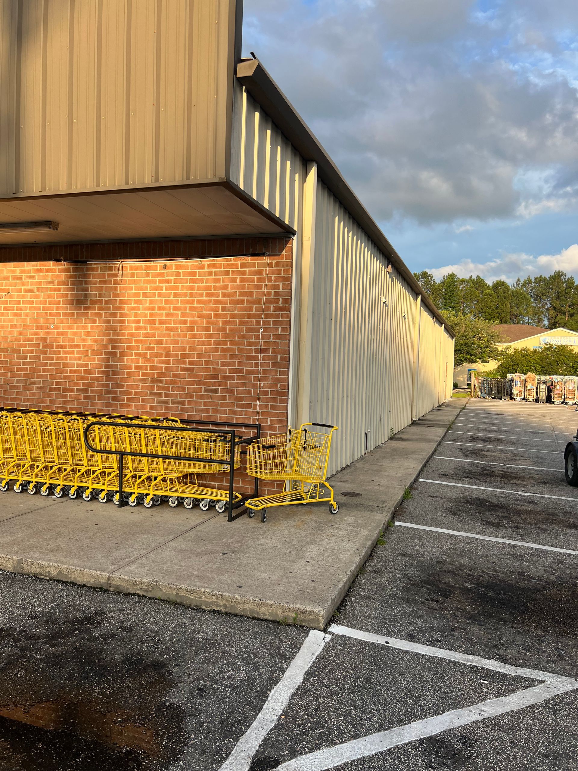 Exterior of a brick building with yellow shopping carts lined up on a concrete sidewalk, with a parking lot visible.