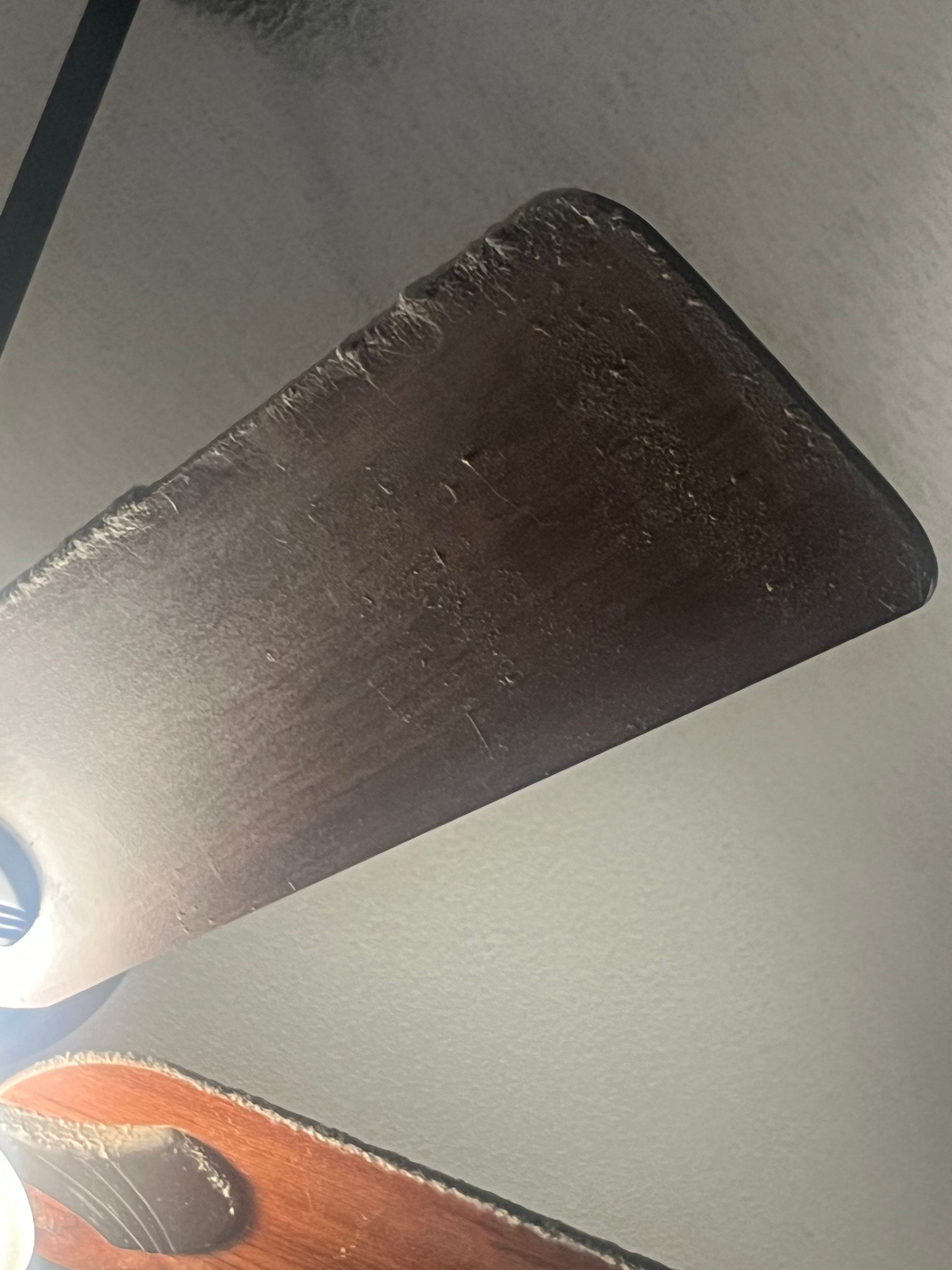 Close-up of a dusty, brown ceiling fan blade against a white ceiling.