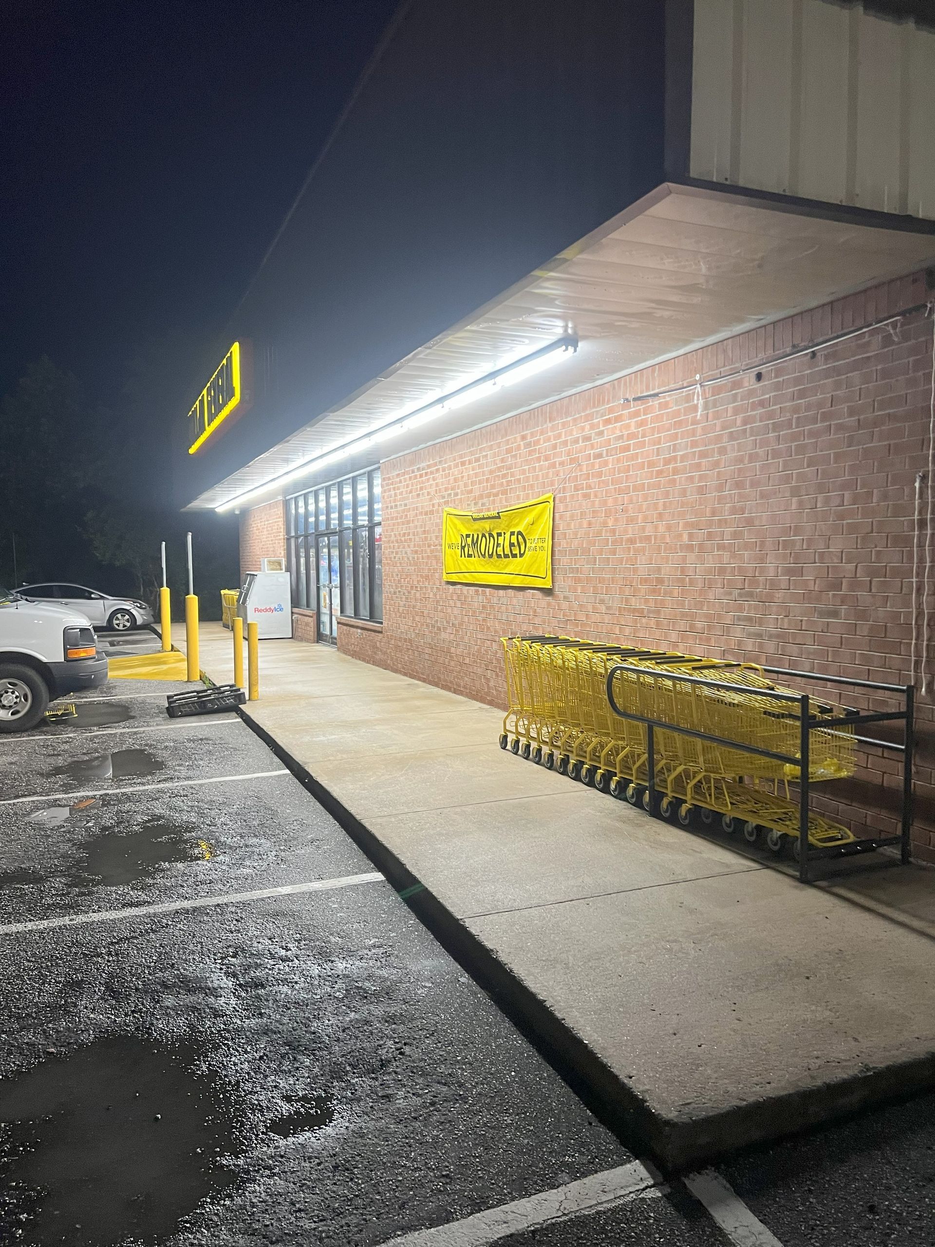 Exterior of a Dollar General store at night. A concrete ramp leads to the entrance. Shopping carts are lined up.