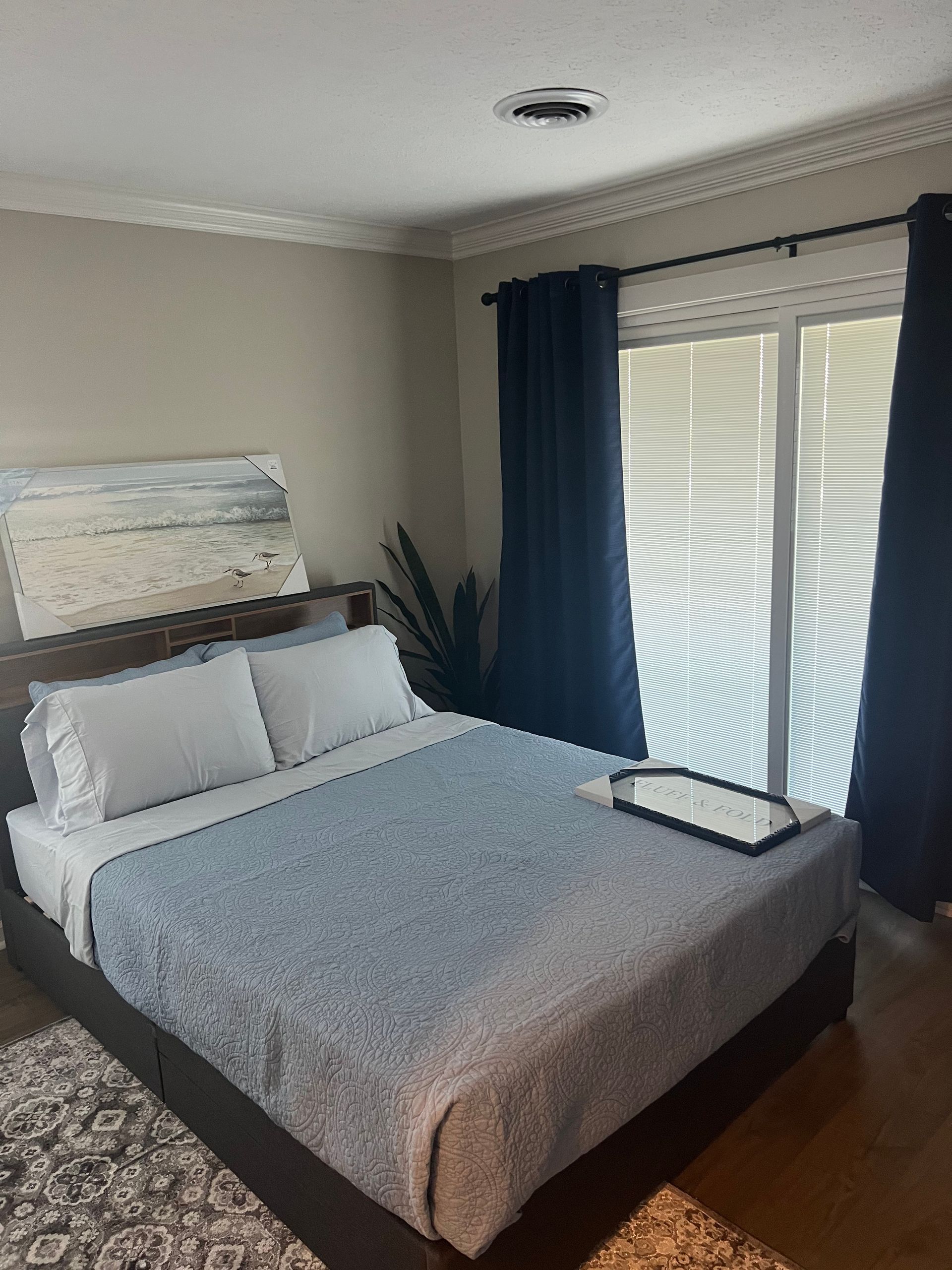 Bedroom with a bed, blue bedding, a window with dark blue curtains, and art.