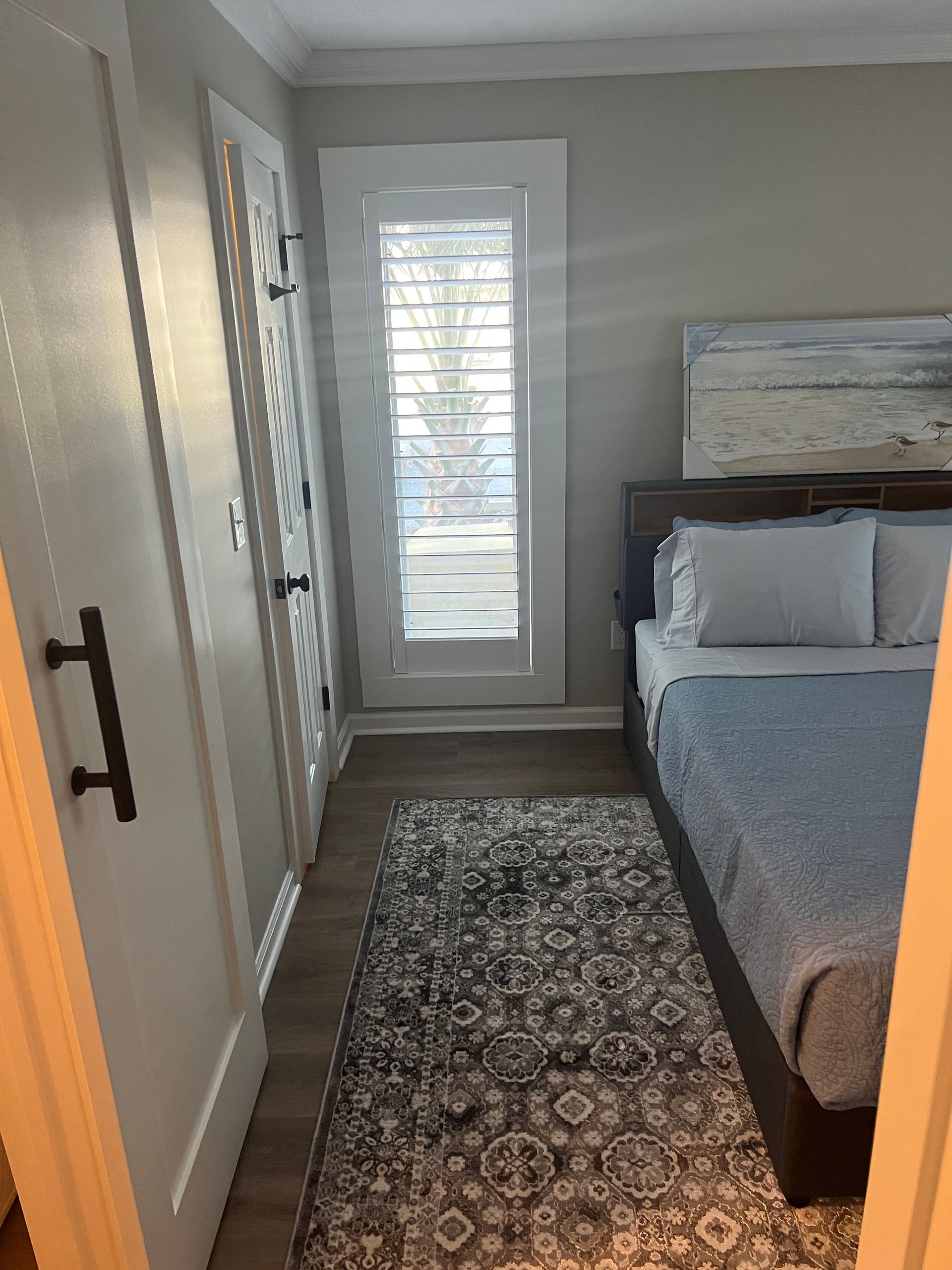 Bedroom with a bed, rug, window with shutters, and closet. Gray walls, light-colored floor, blue bedding, and dark wood bed frame.