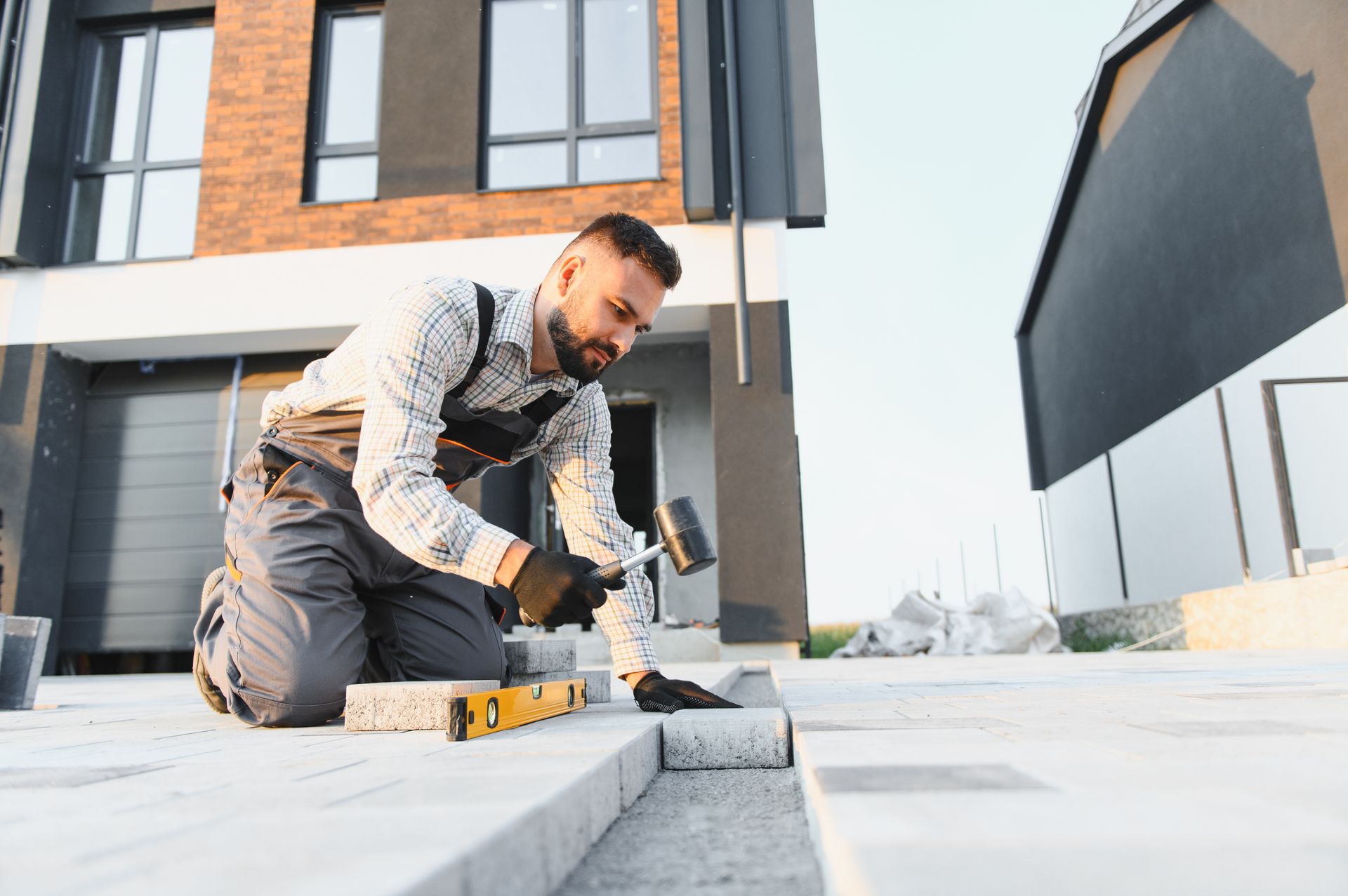 Man kneeling, using a mallet on a paver, building a patio outdoors.