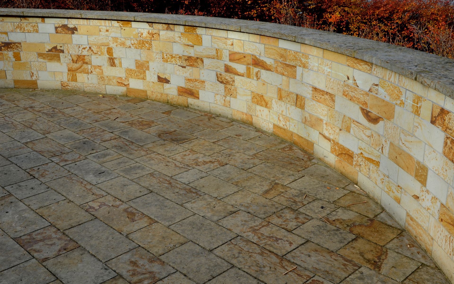 Curved sandstone brick wall and matching ground, outdoor setting.