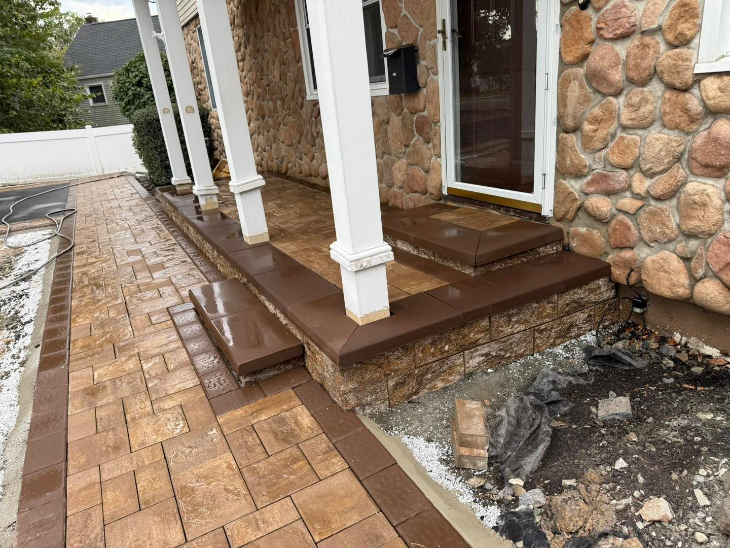 Workers laying pavers on a gravel bed, outdoors. One kneels, placing a paver; two others stand nearby.